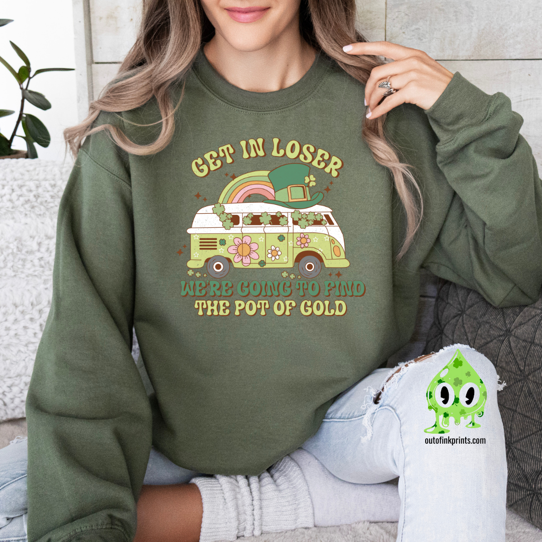 A woman wearing a green sweatshirt with a St. Patrick's Day theme, featuring text and a graphic of a rainbow, clover, and what appears to be a leprechaun.