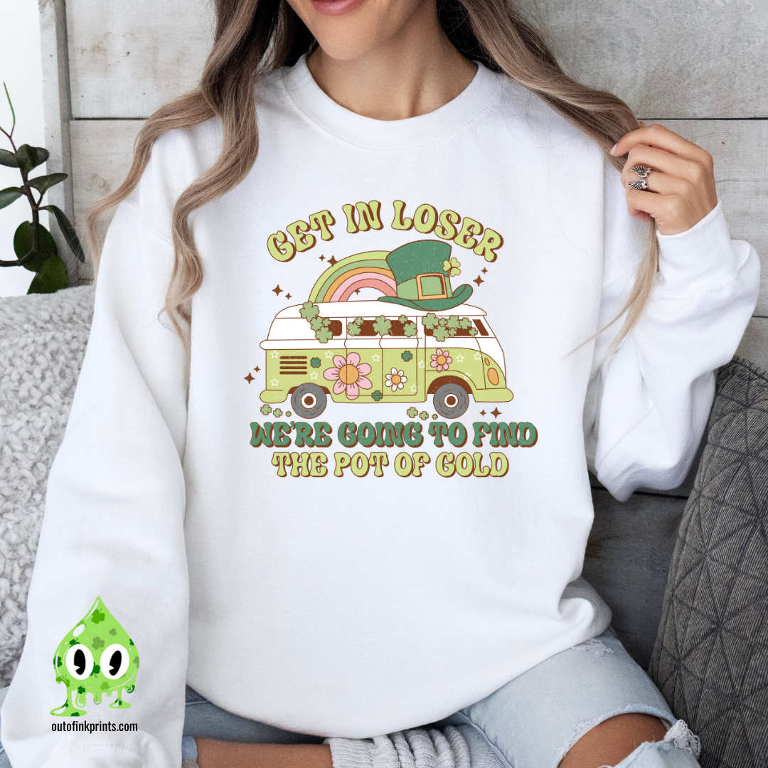 A woman wearing a white sweatshirt with a St. Patrick's Day theme, featuring text and a graphic of a rainbow, clover, and what appears to be a leprechaun.