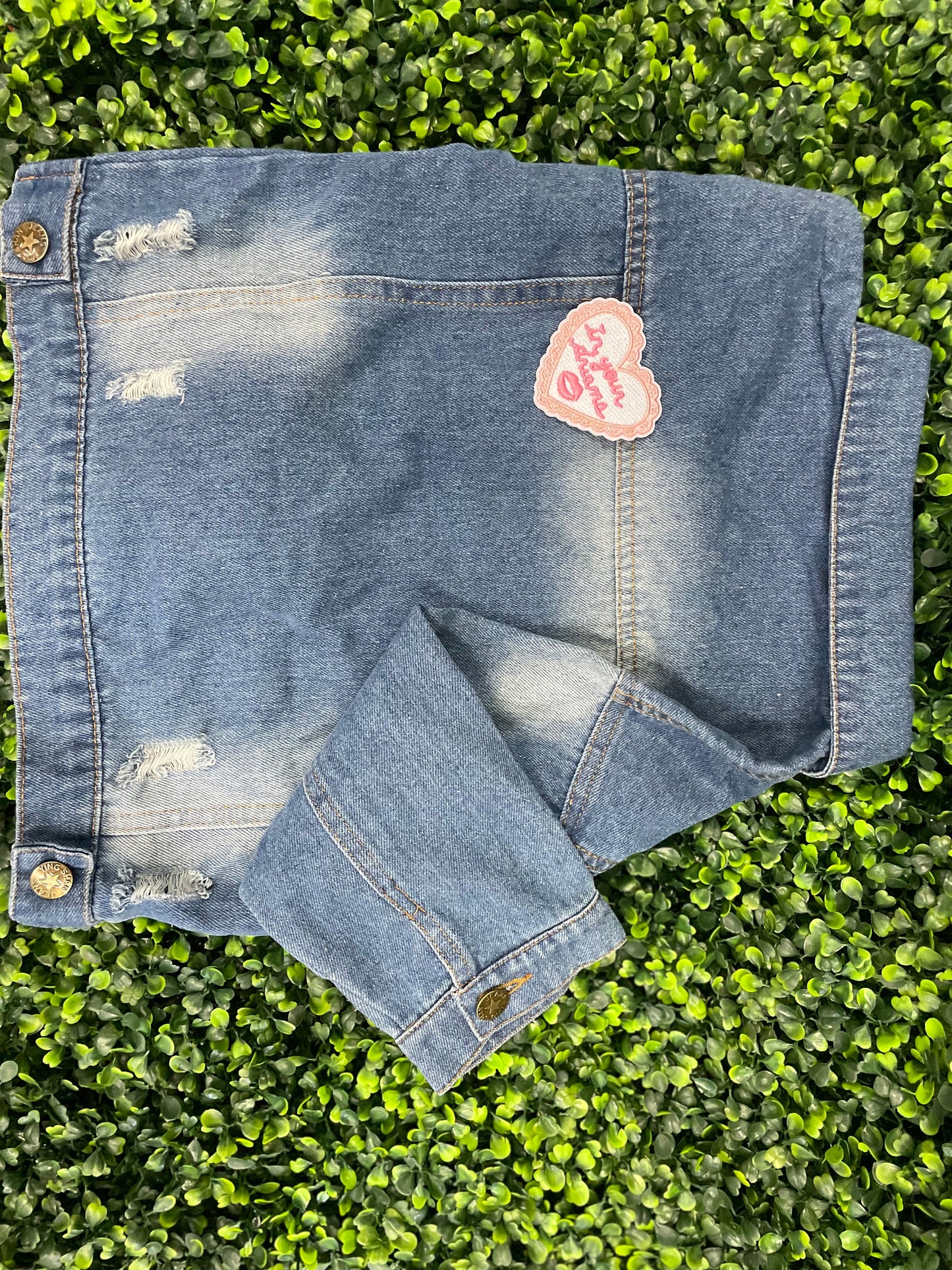Heart-shaped embroidered patch with 'In your dreams' text held against a children's denim jean jacket