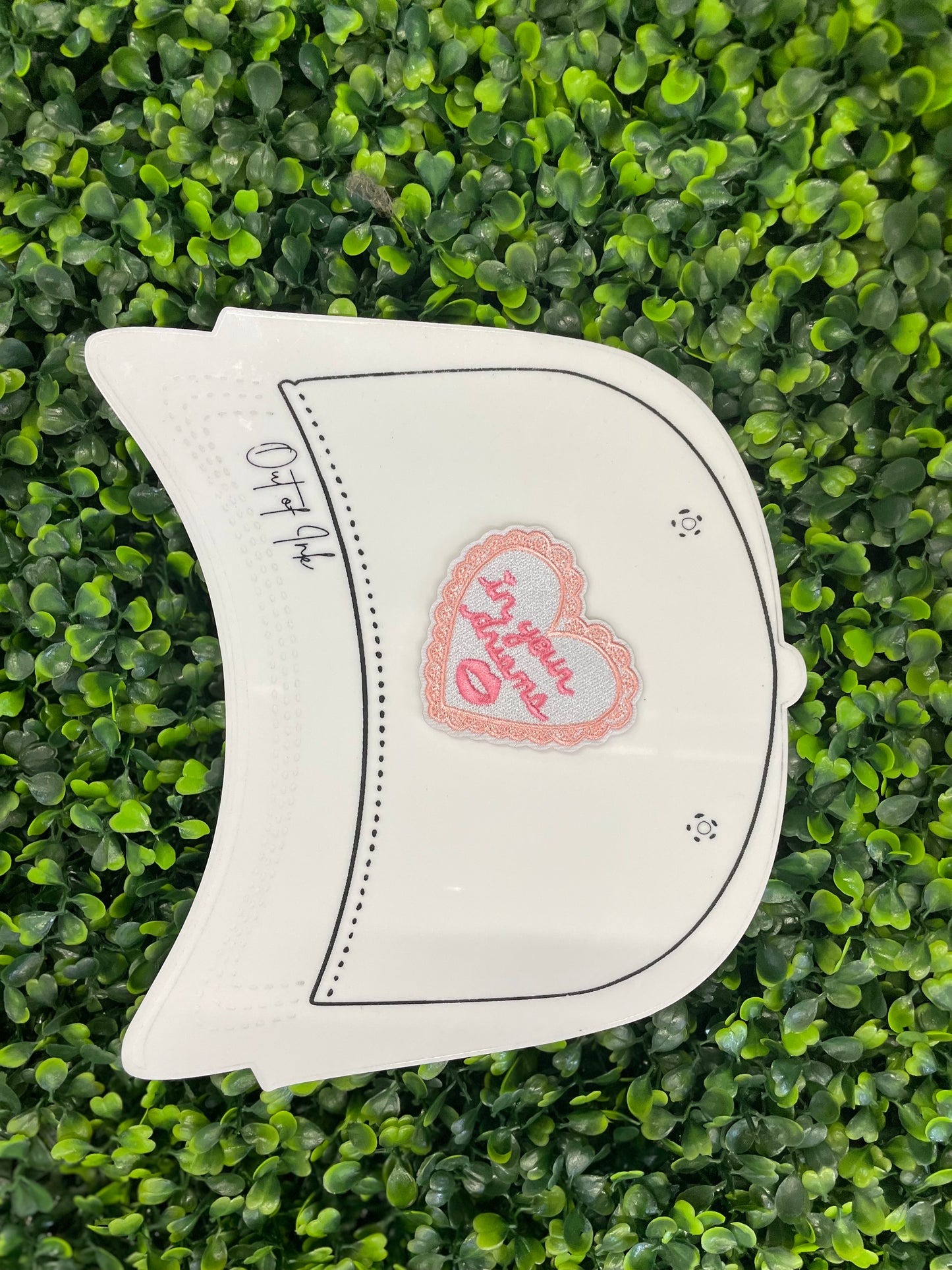Heart-shaped embroidered patch with 'In your dreams' text held against a white trucker hat graphic