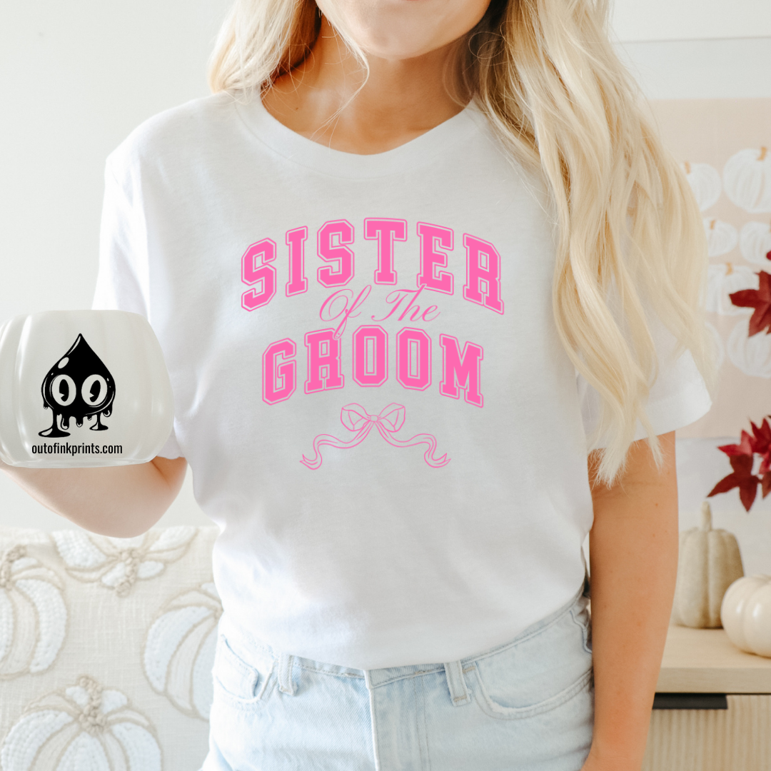 A woman smiling and wearing a white shirt with 'Sister of the Groom' text and a pink bow design on it.
