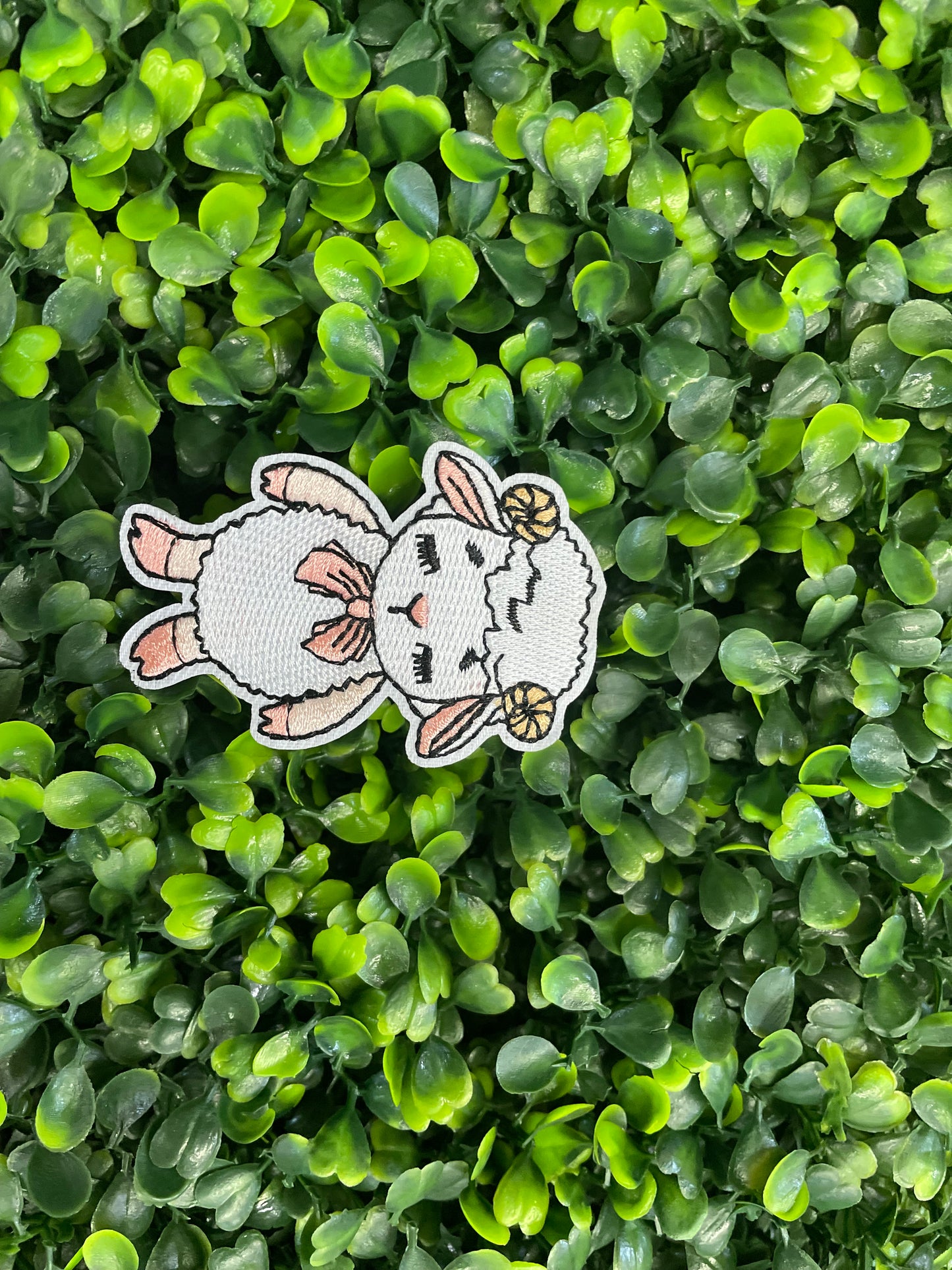 Patch of a cartoon sheep with a bow on a green leafy background