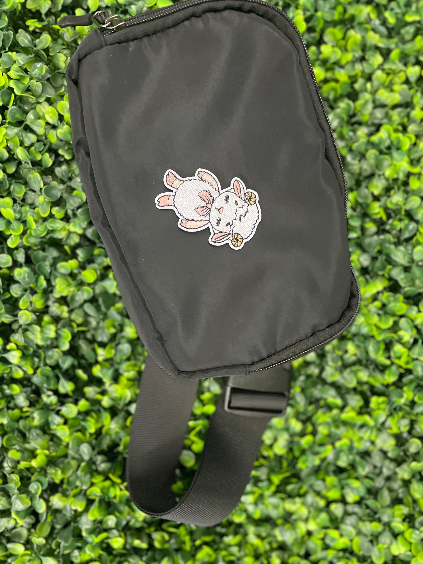 Patch of a cartoon lamb held against a black shoulder bag