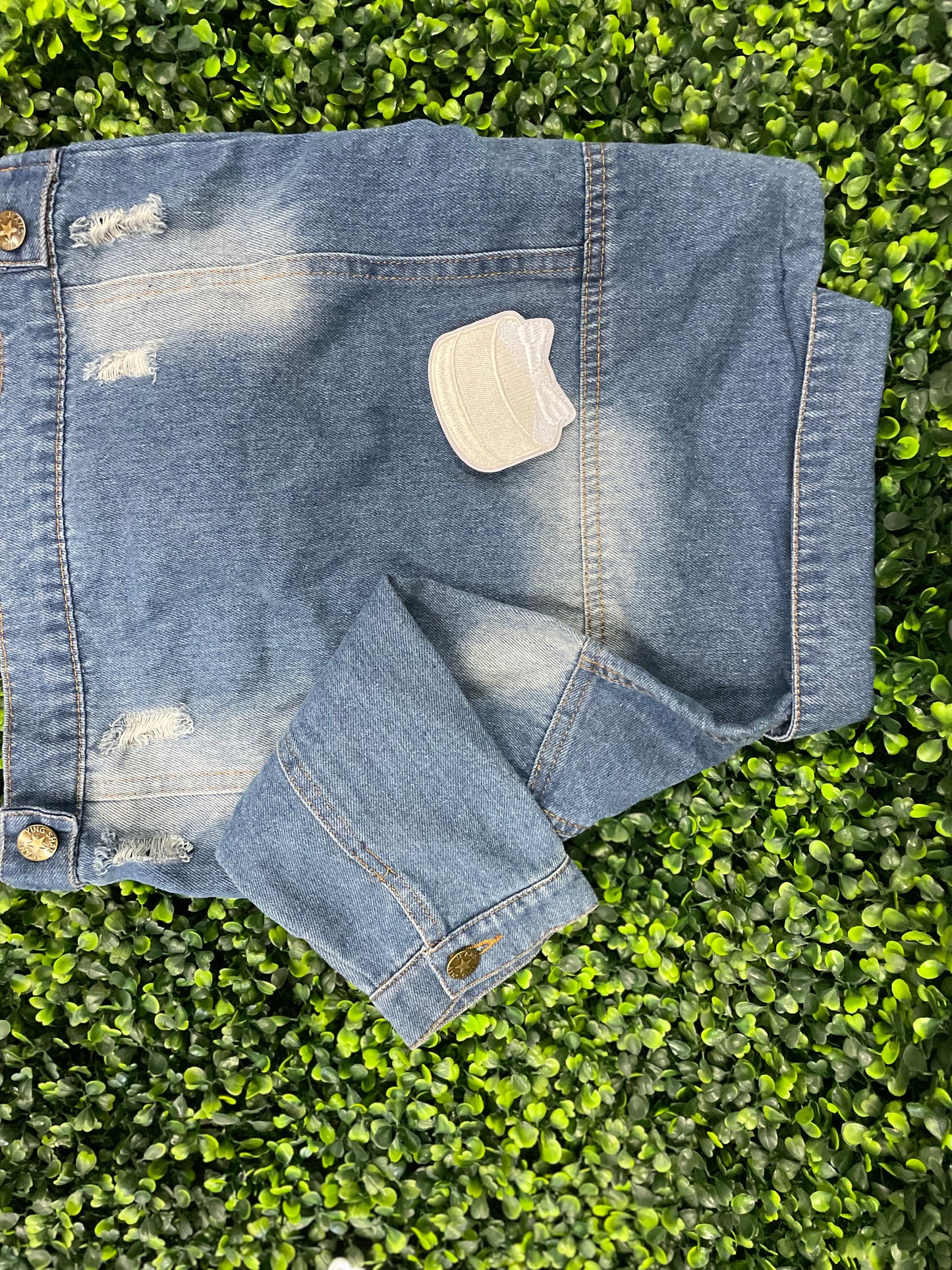 Embroidered patch of a white cake with a white bow placed on top, placed on a children's denim jean jacket