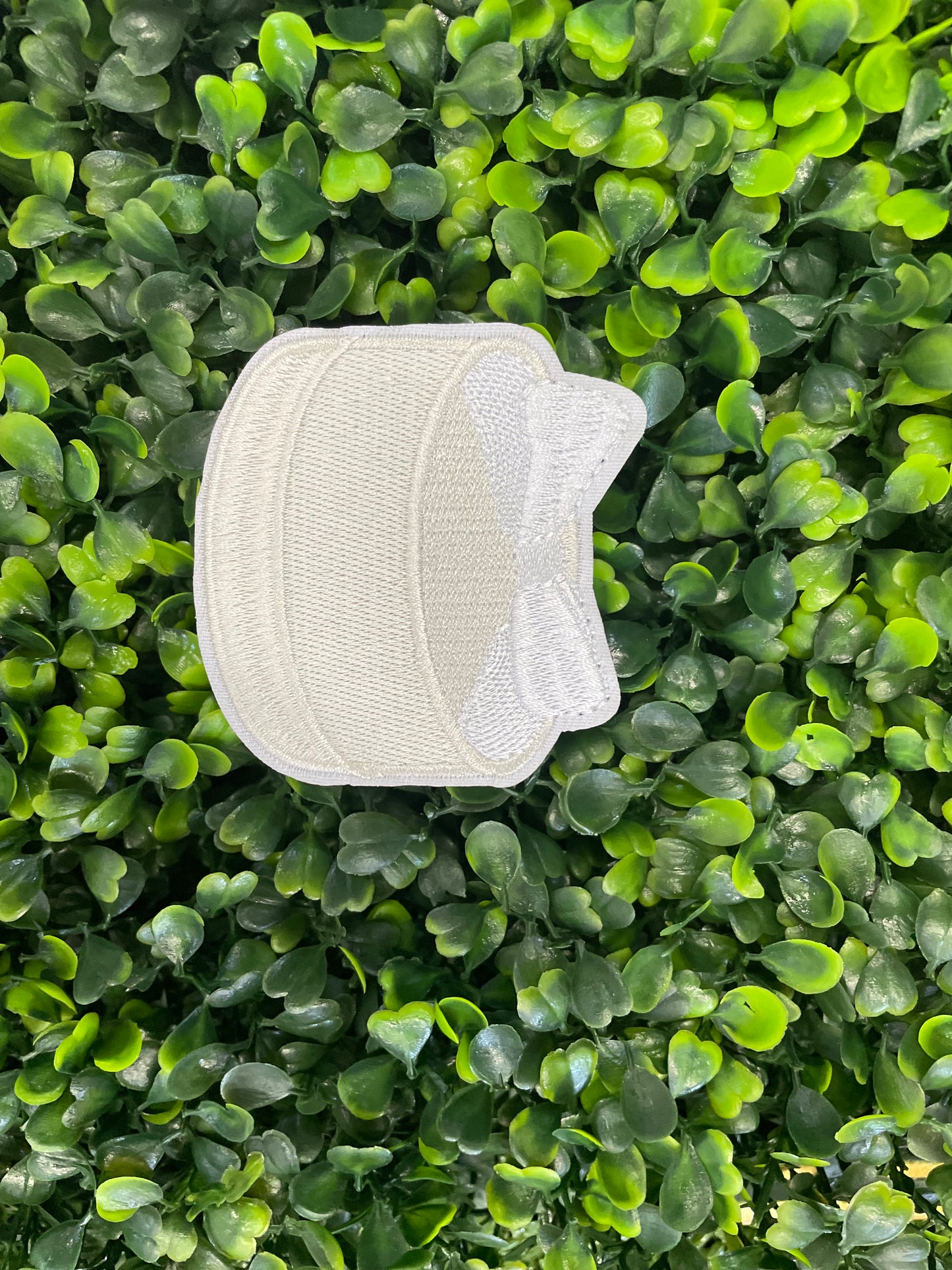 Embroidered patch of a white cake with a white bow placed on top, placed on a green leafy background