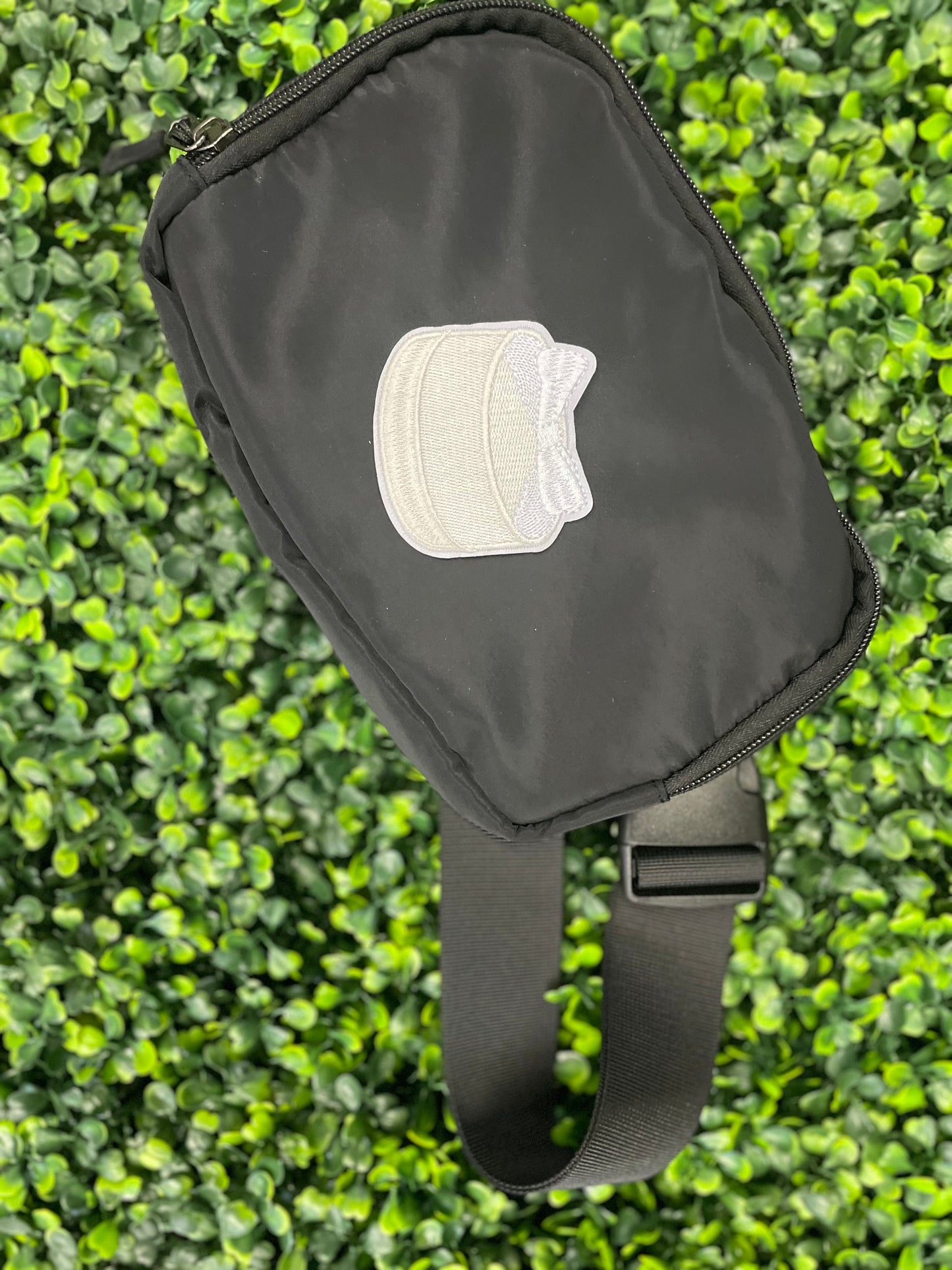 Embroidered patch of a white cake with a white bow placed on top, placed on a black shoulder bag