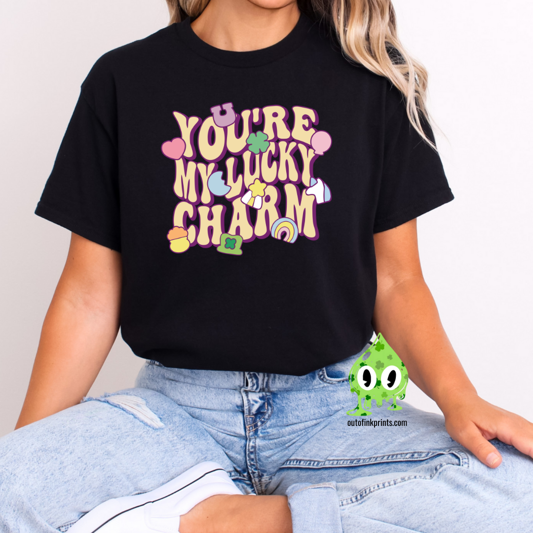 Front view of a black t-shirt with the text 'YOU'RE MY LUCKY CHARM' in a playful font, surrounded by decorative elements like shamrocks and hearts.