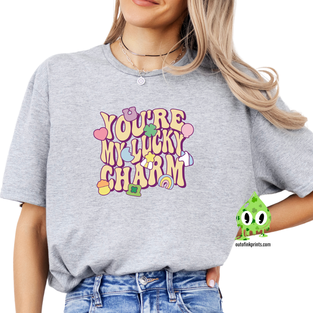 Front view of a gray t-shirt with the text 'YOU'RE MY LUCKY CHARM' in a playful font, surrounded by decorative elements like shamrocks and hearts.
