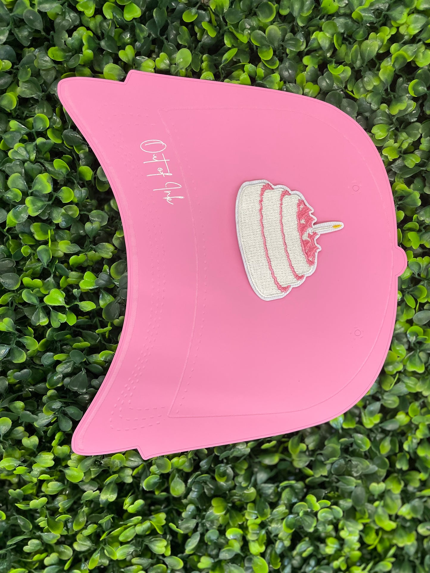A small pink and white birthday cake embroidered patch placed on top of a pink trucker hat graphic
