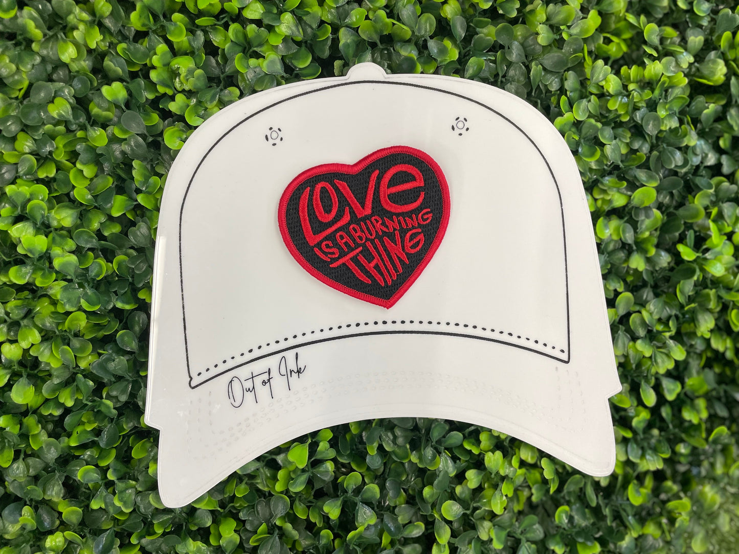 Heart-shaped patch with 'Love is a Burning Thing' text, placed on a white trucker hat