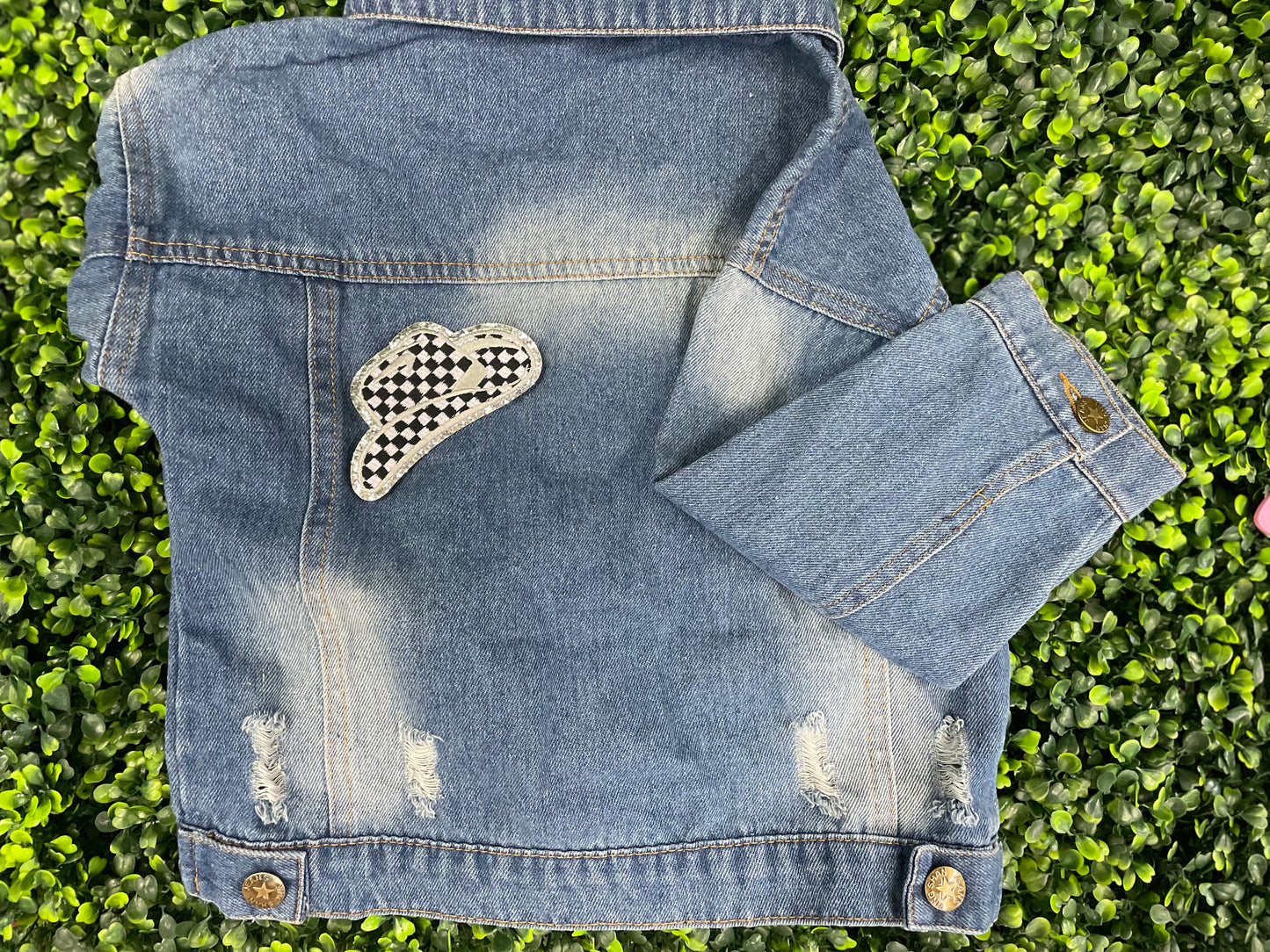 Checkered white and black cowboy hat patch with silver lining, placed onto a children's denim jean jacket