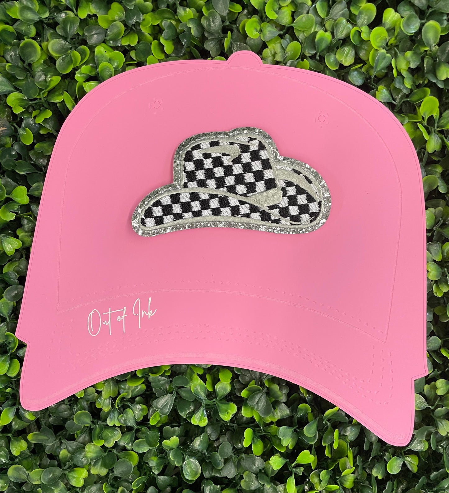 Checkered white and black cowboy hat patch with silver lining, placed onto a pink trucker hat graphic