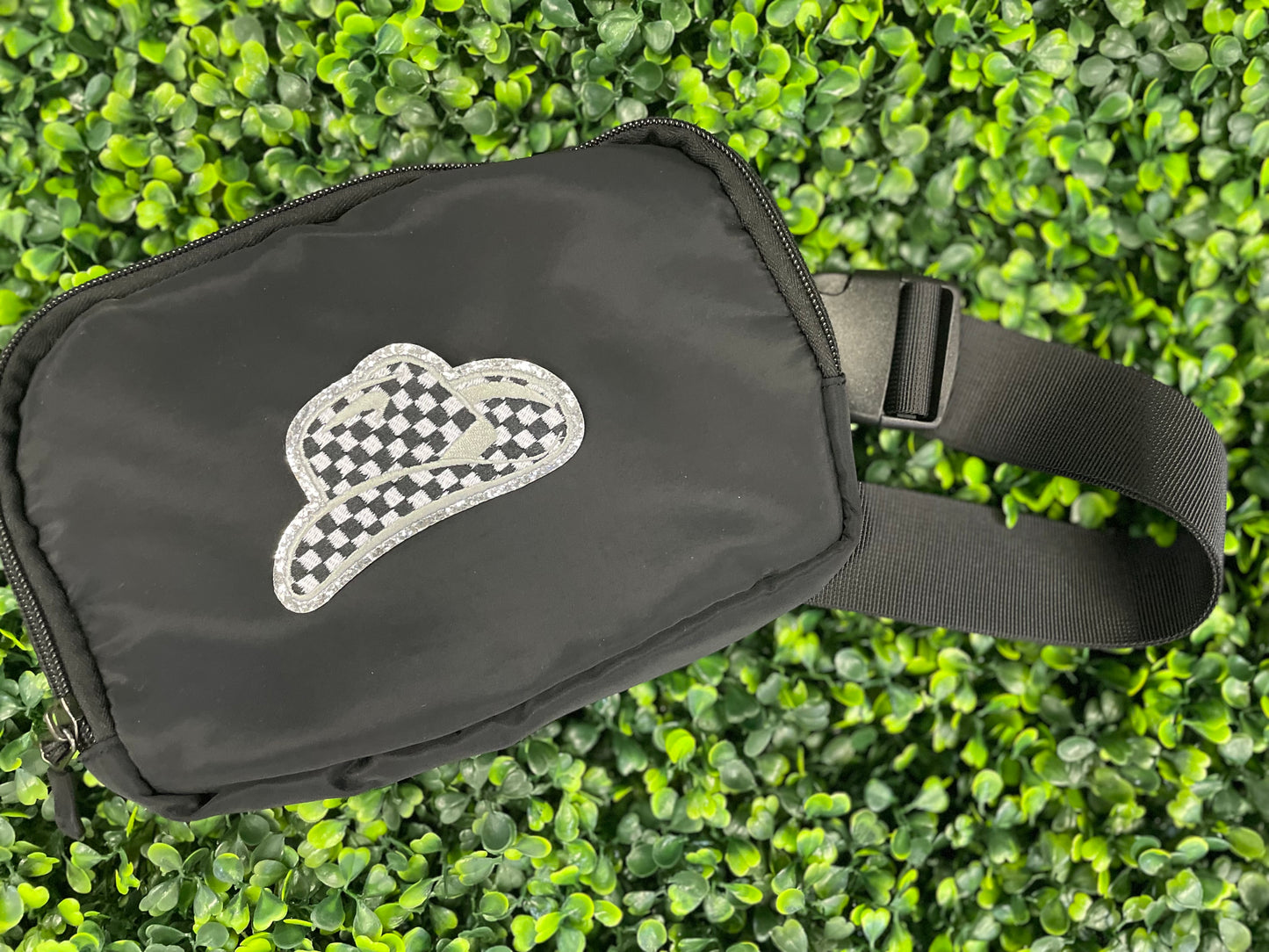 Checkered white and black cowboy hat patch with silver lining, placed on a black fanny pack