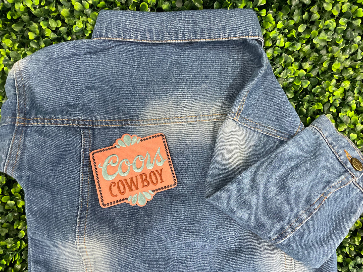 Embroidered patch with 'Coors Cowboy' text on a light orange background with teal accents, placed on a children's denim jean jacket