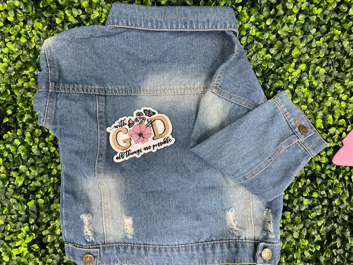 Embroidered patch butterflies and flowers and text stating "with God all things are possible", held against a children's jean jacket