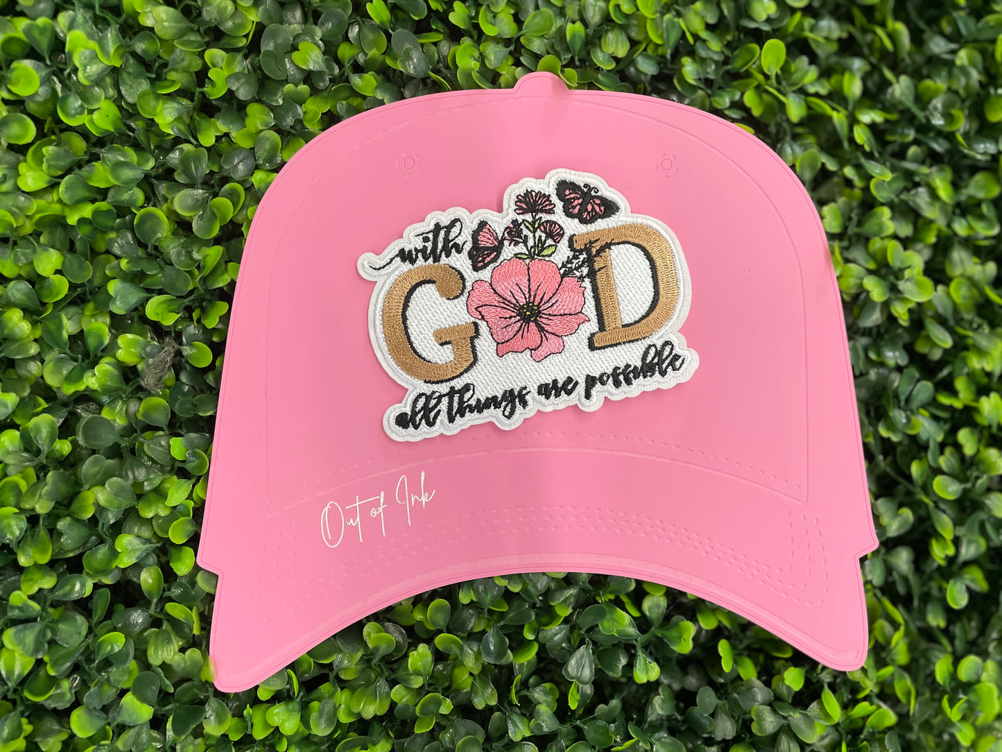 Embroidered patch butterflies and flowers and text stating "with God all things are possible", held against a green leafy background