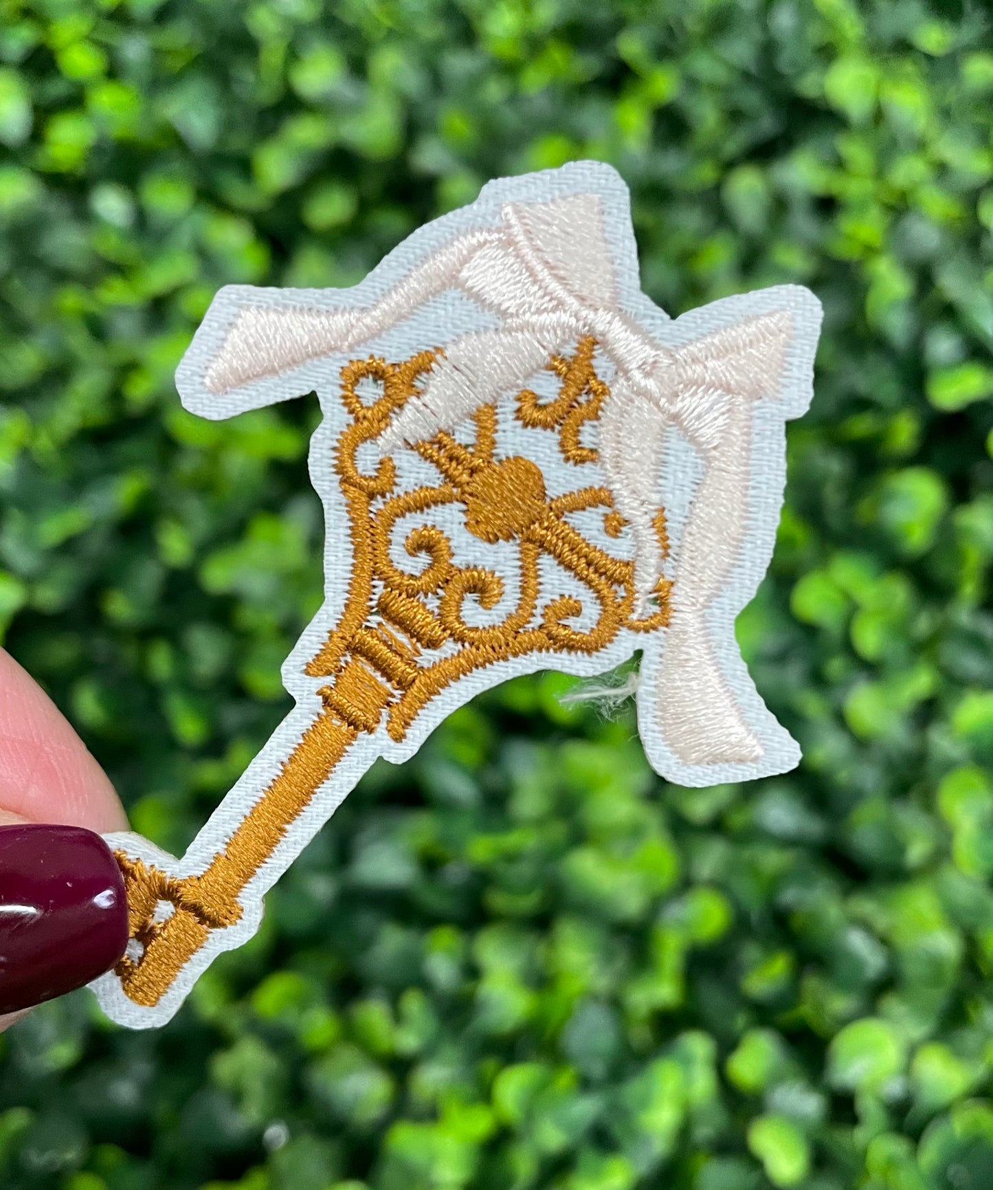 A patch in the shape of a vintage key with a gold bow, embroidery work, on a white background.