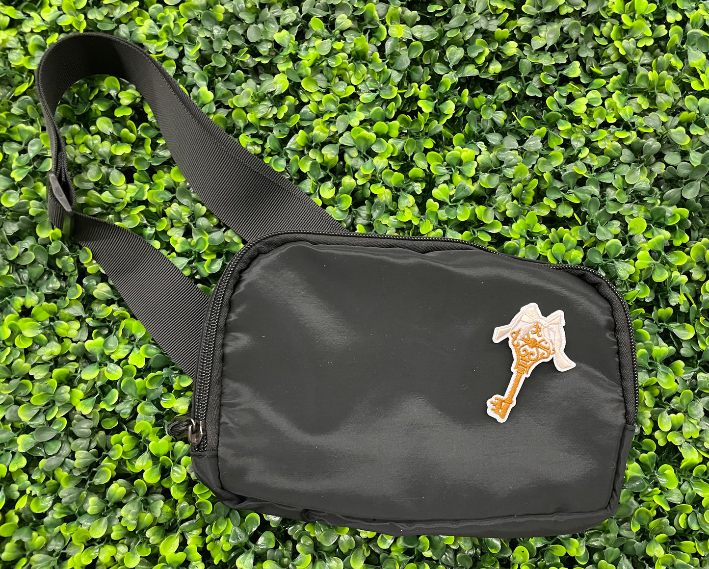 A patch in the shape of a vintage key with a gold bow, embroidery work, on a black shoulder bag