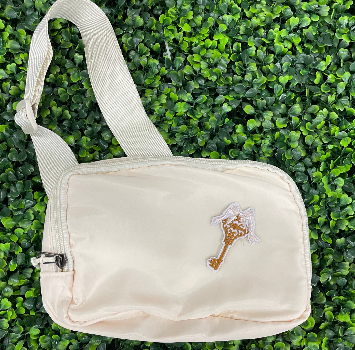 A patch in the shape of a vintage key with a gold bow, embroidery work, on a white shoulder bag