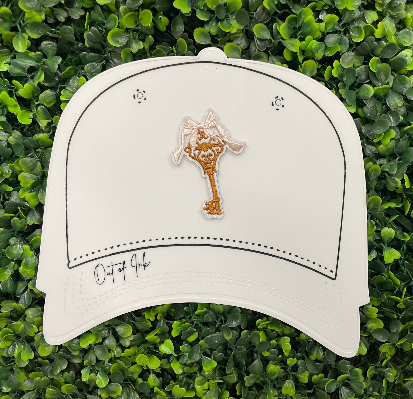 A patch in the shape of a vintage key with a gold bow, embroidery work, set on a white hat graphic