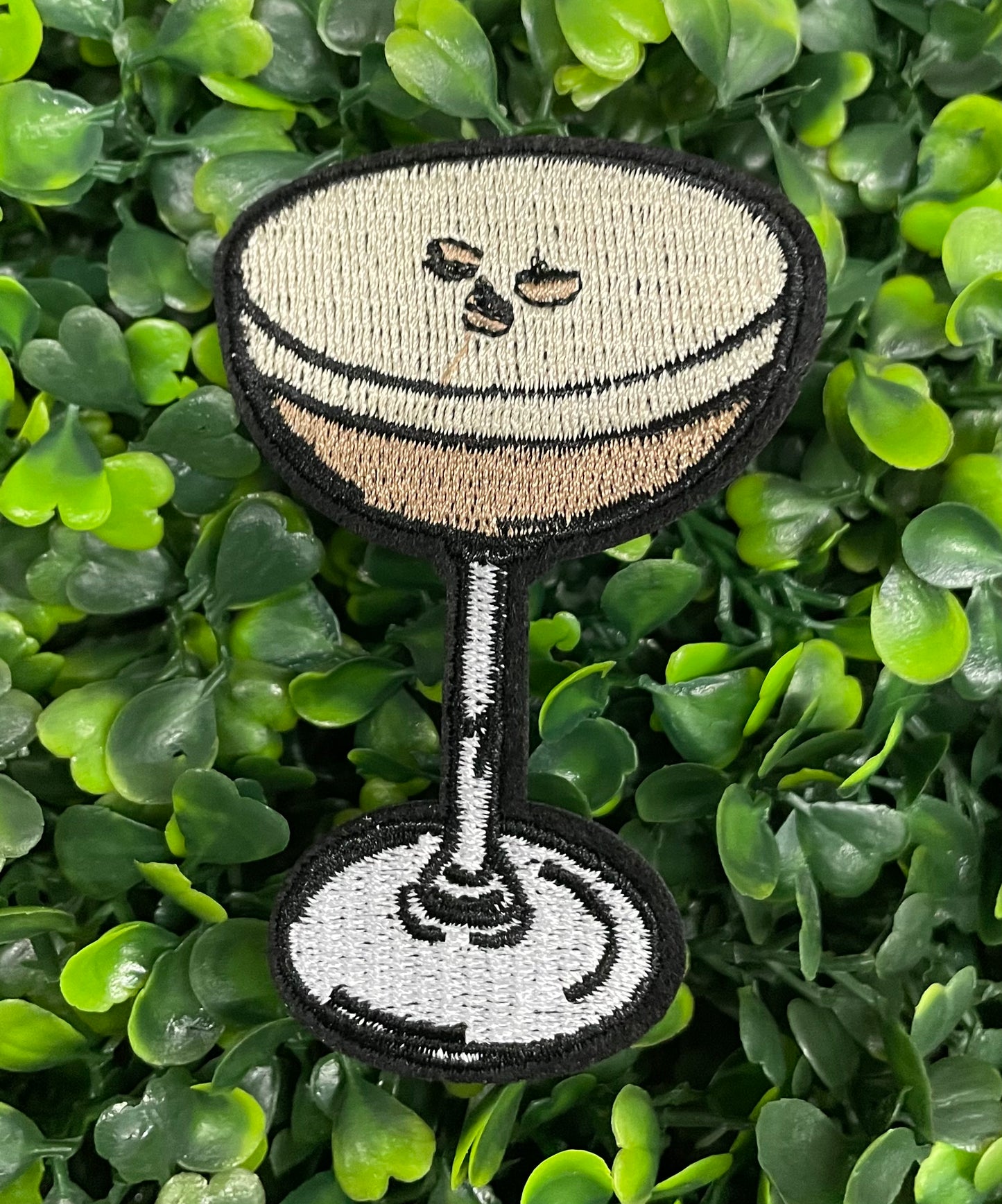 An embroidered martini glass depiction set on a green backdrop