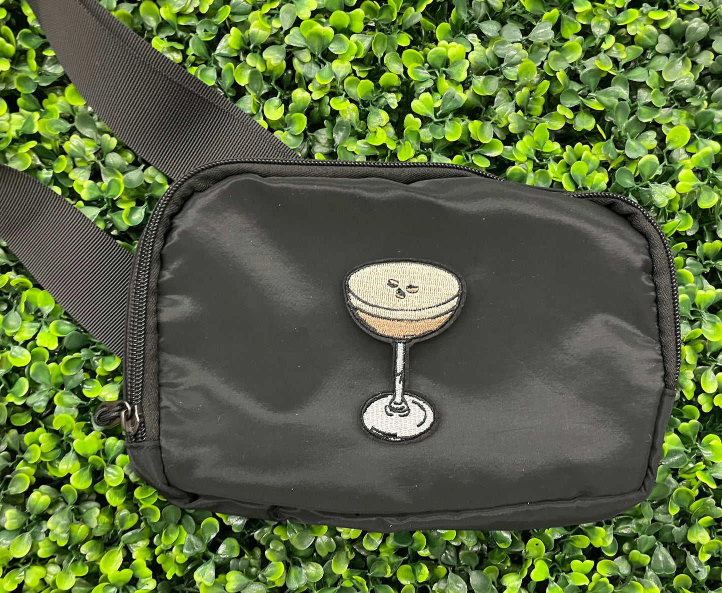 An iron on embroidered martini glass depiction set on a black shoulder bag