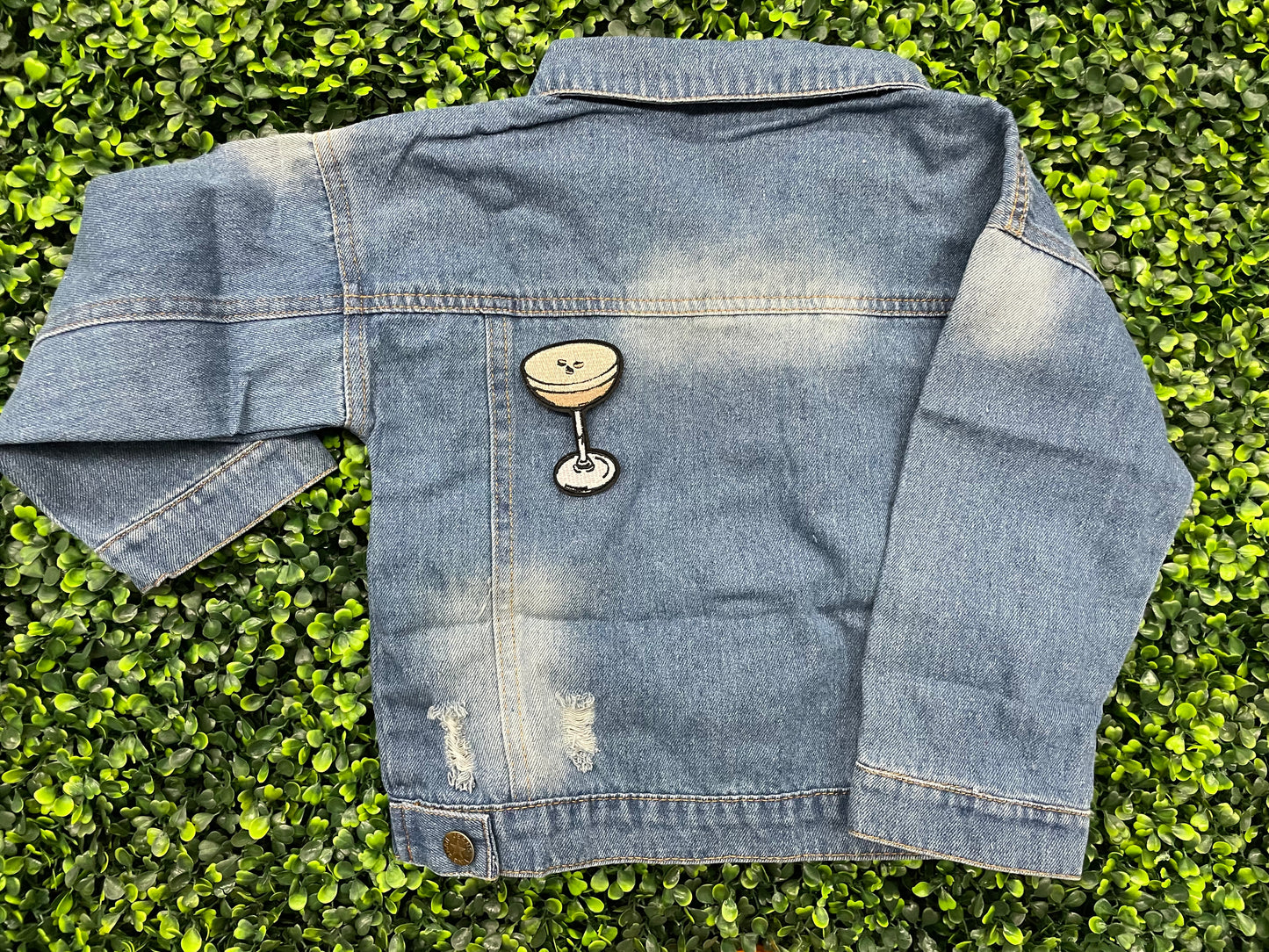 An iron on embroidered martini glass depiction set on a childs jean jacket