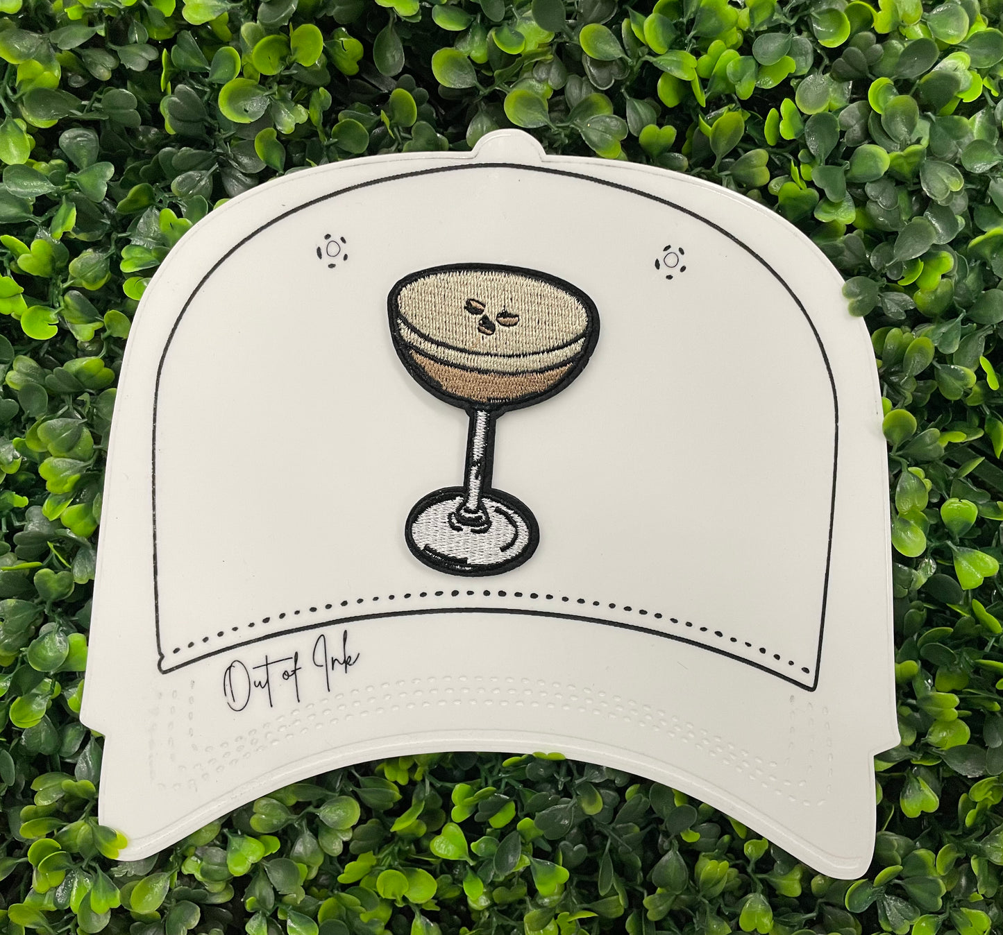 An iron on embroidered martini glass depiction set on a white hat