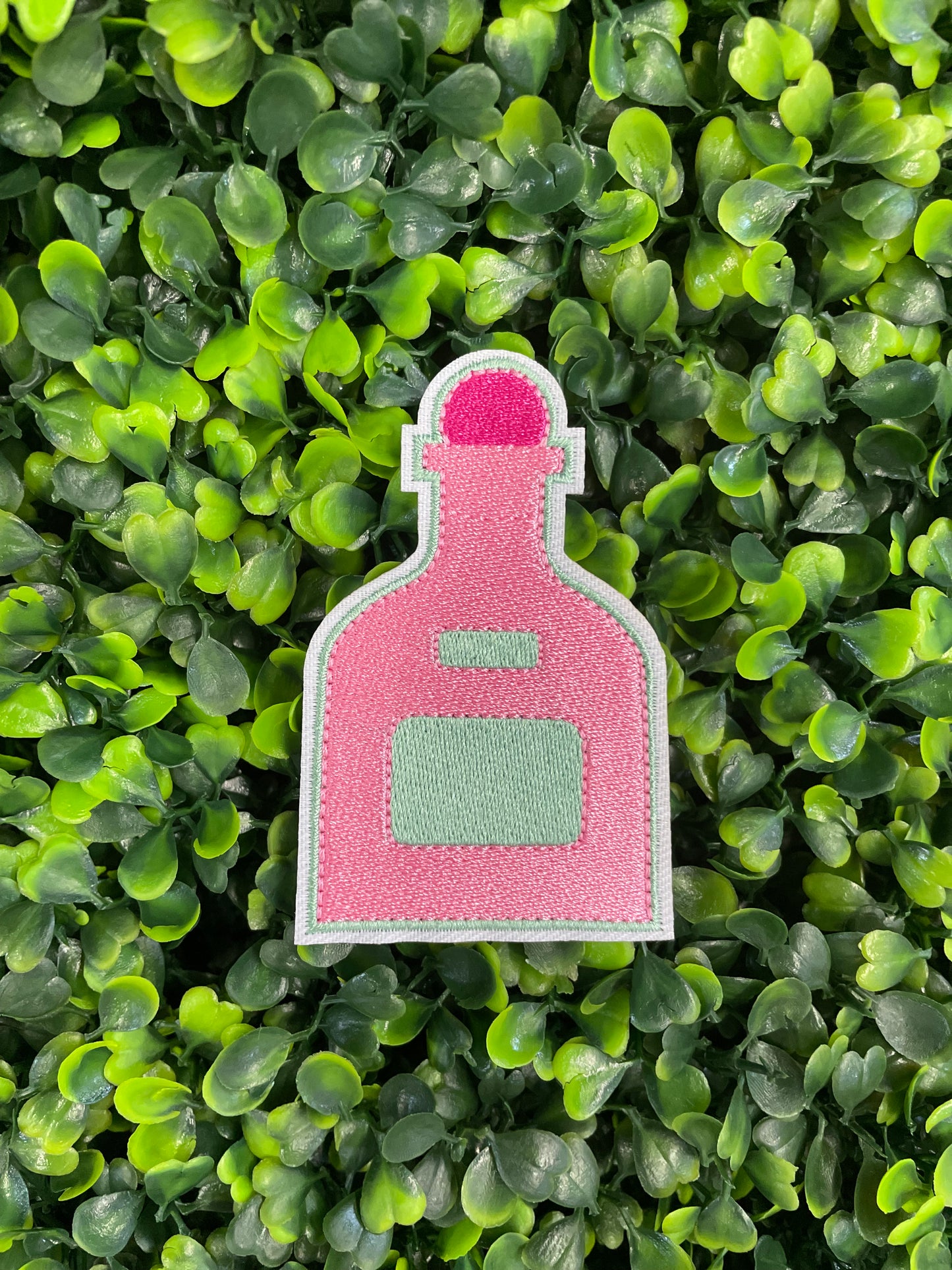 A pink bottle-shaped patch held against a green leafy background