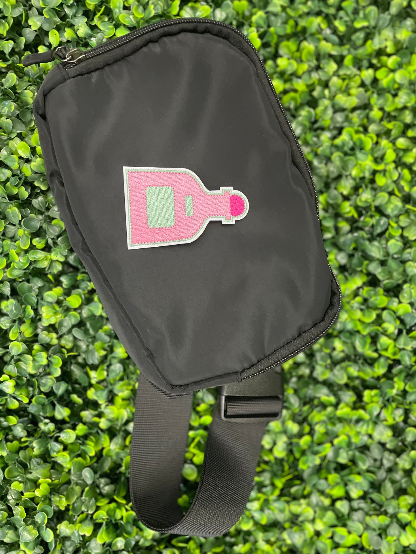 Pink bottle-shaped patch held against a black shoulder bag