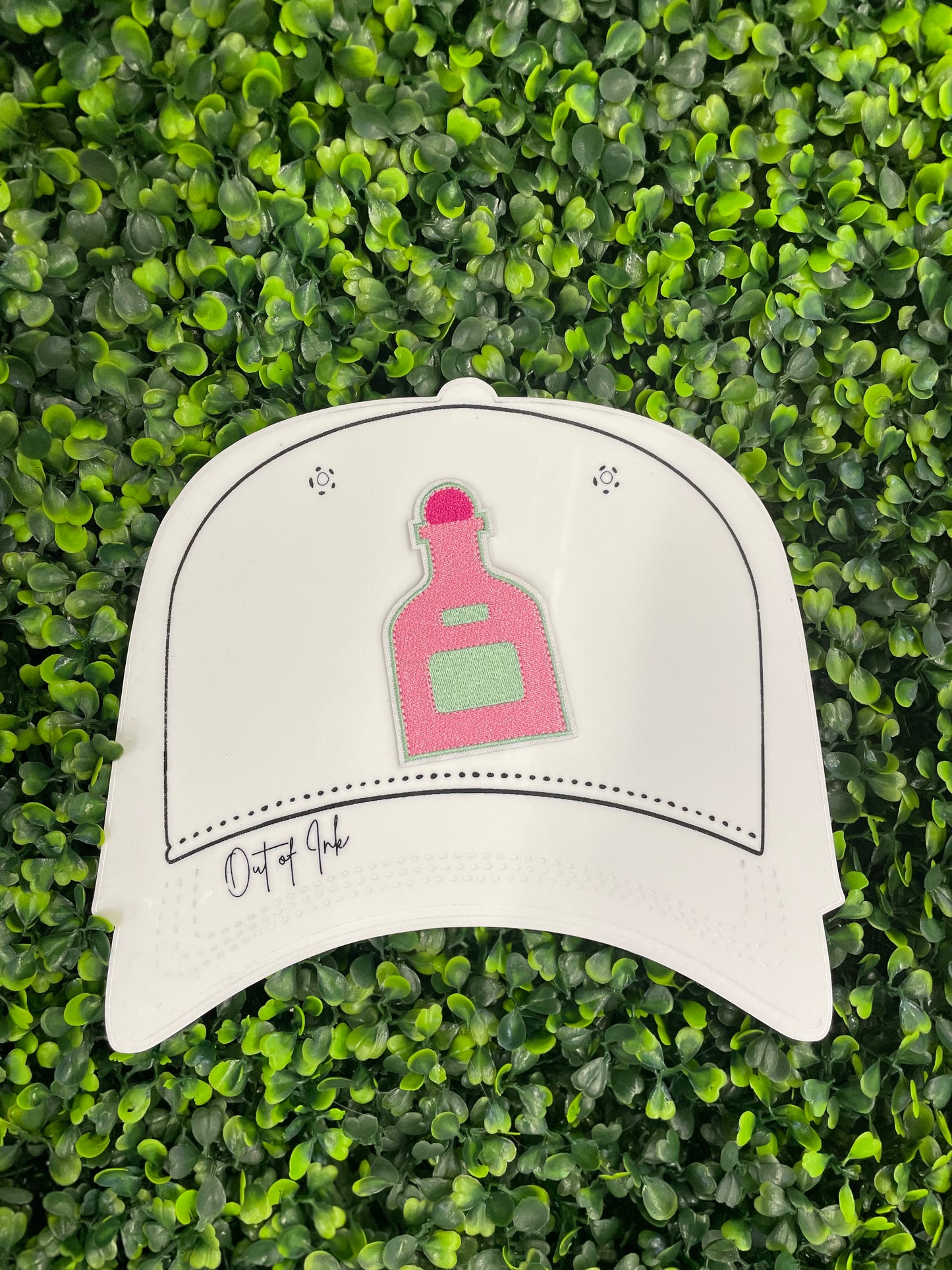 Pink bottle-shaped patch held against a white trucker hat graphic