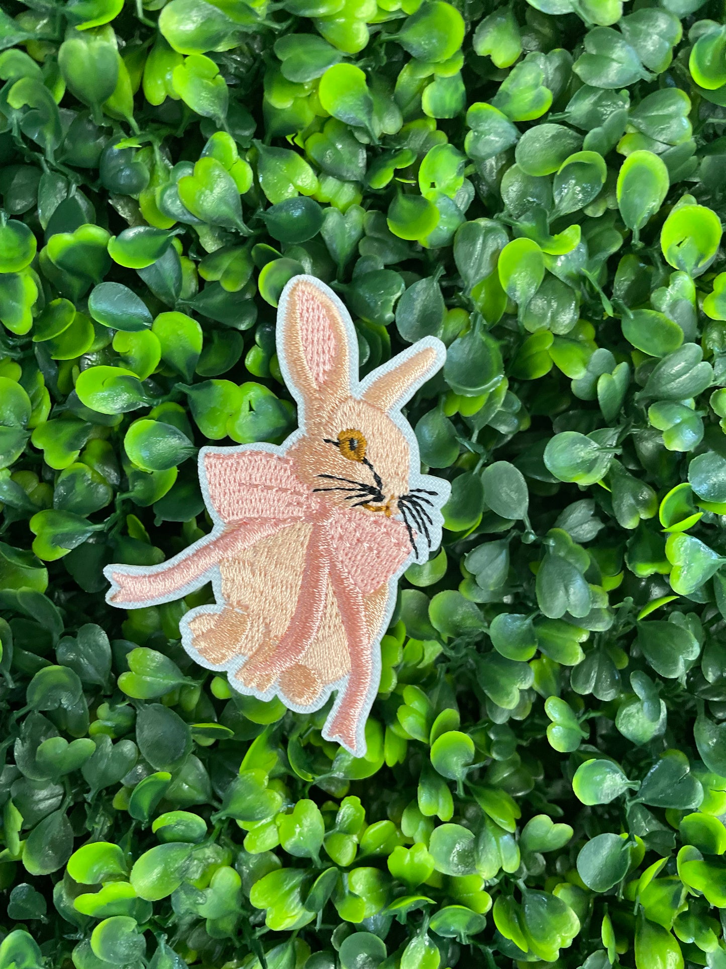 Embroidered patch of a pink bunny white a pink bow placed against a green and leafy background