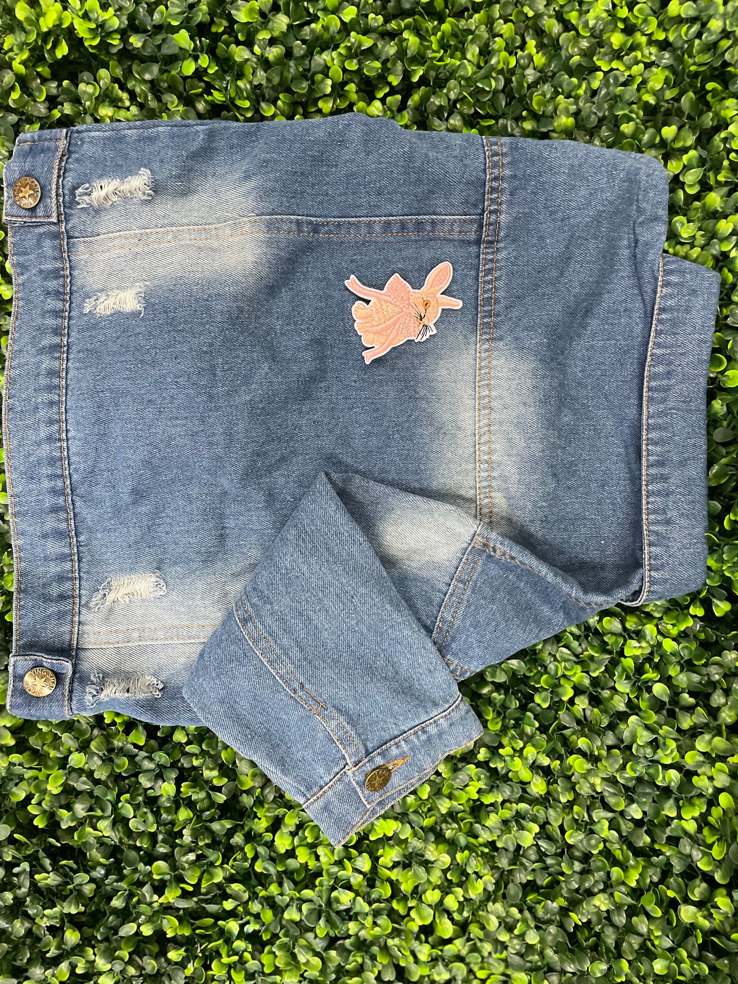 Embroidered patch of a pink bunny white a pink bow placed on a child's denim jean jacket