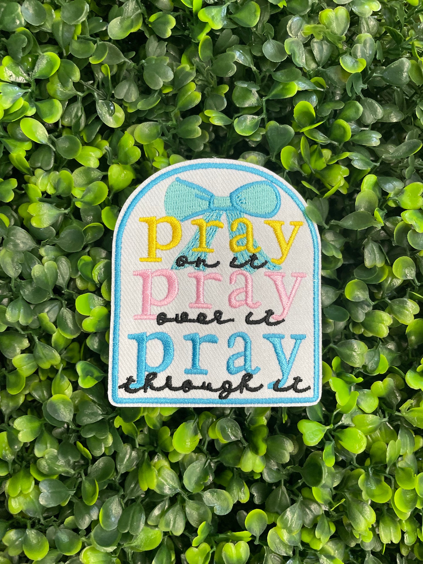 Embroidered patch with 'pray on it, pray over it, pray through it' text in various colors placed on a green and leafy background