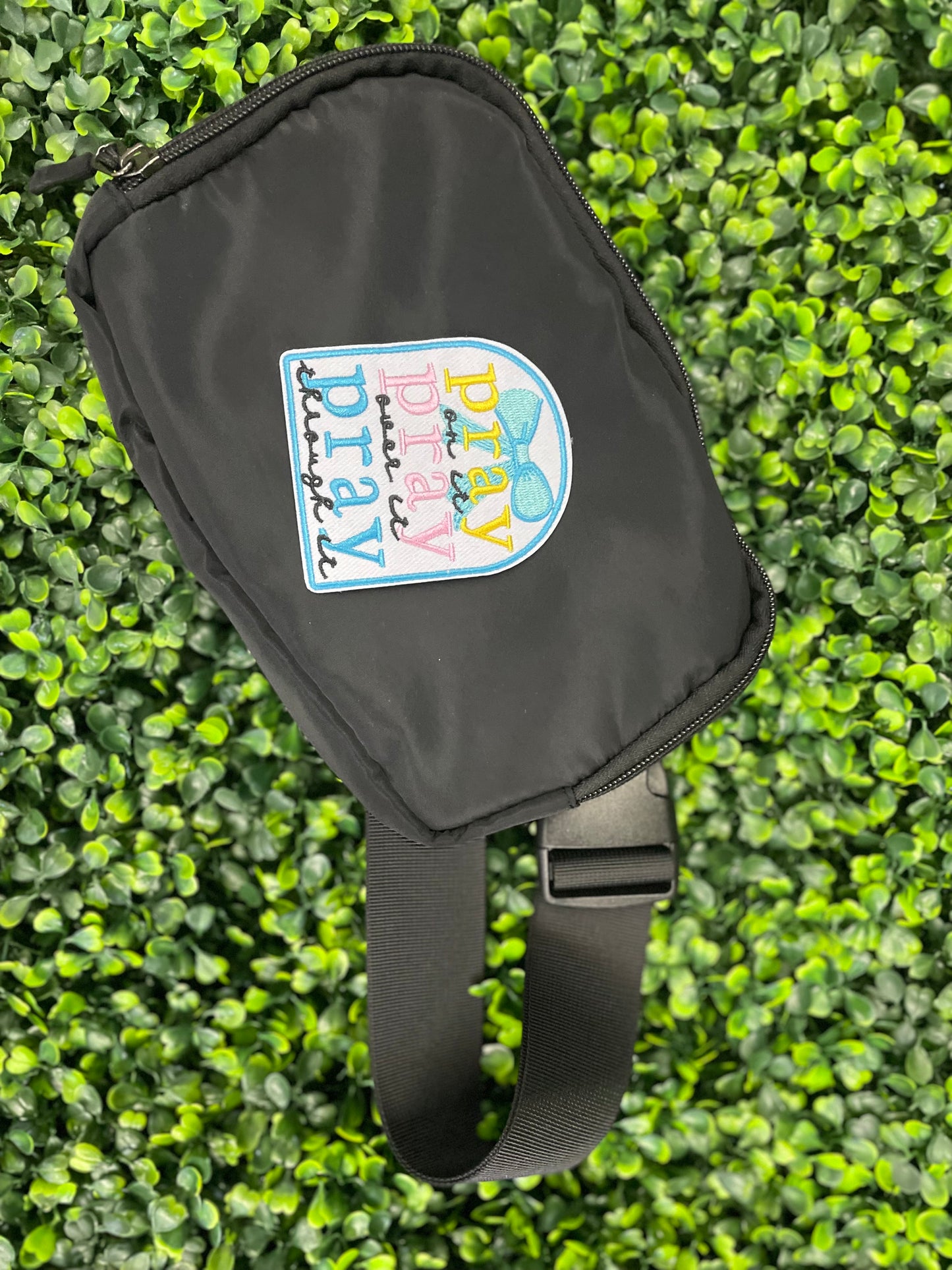 Embroidered patch with 'pray on it, pray over it, pray through it' text in various colors placed on top of a black fanny pack