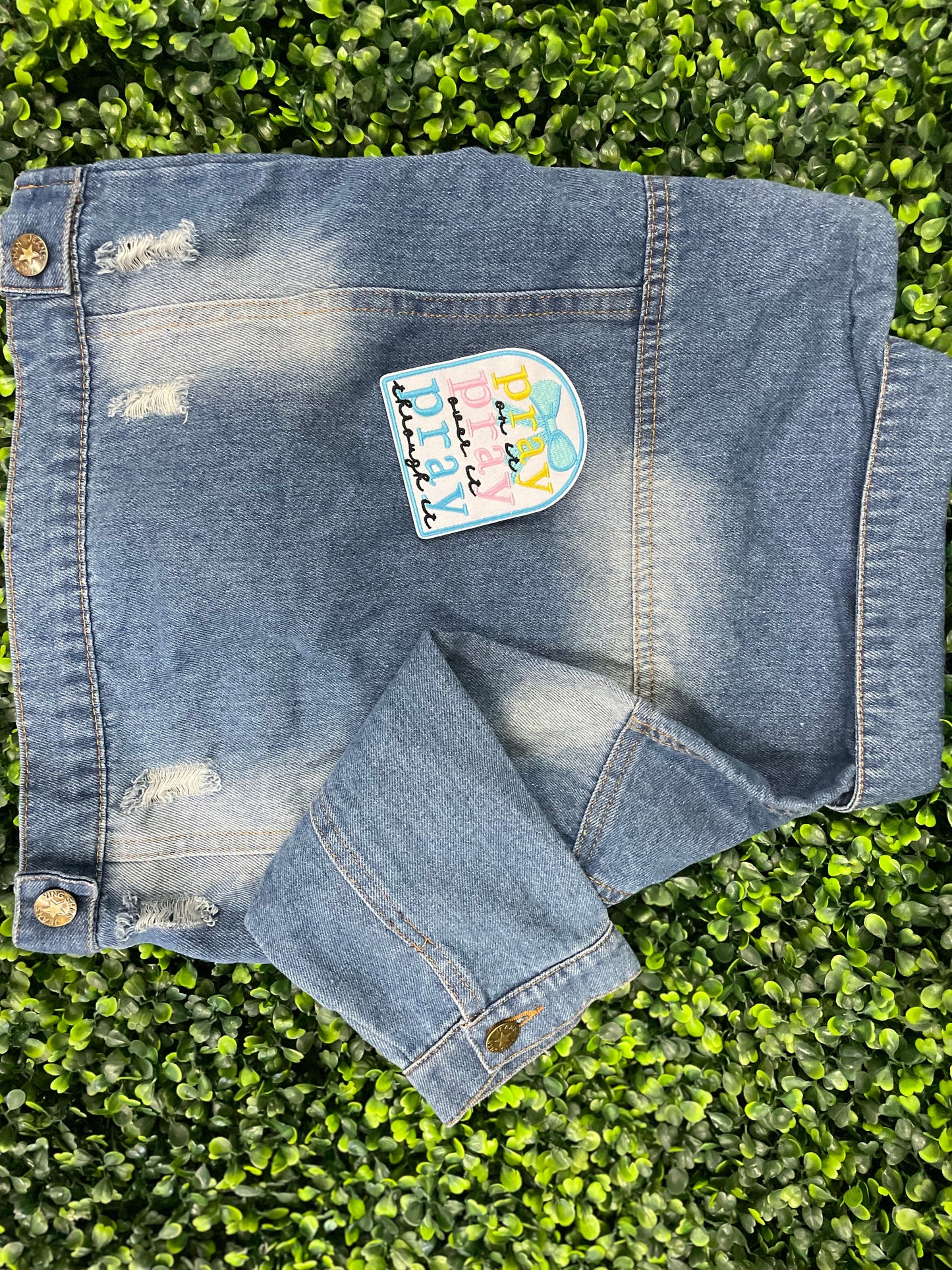 Embroidered patch with 'pray on it, pray over it, pray through it' text in various colors placed on a children's denim jean jacket