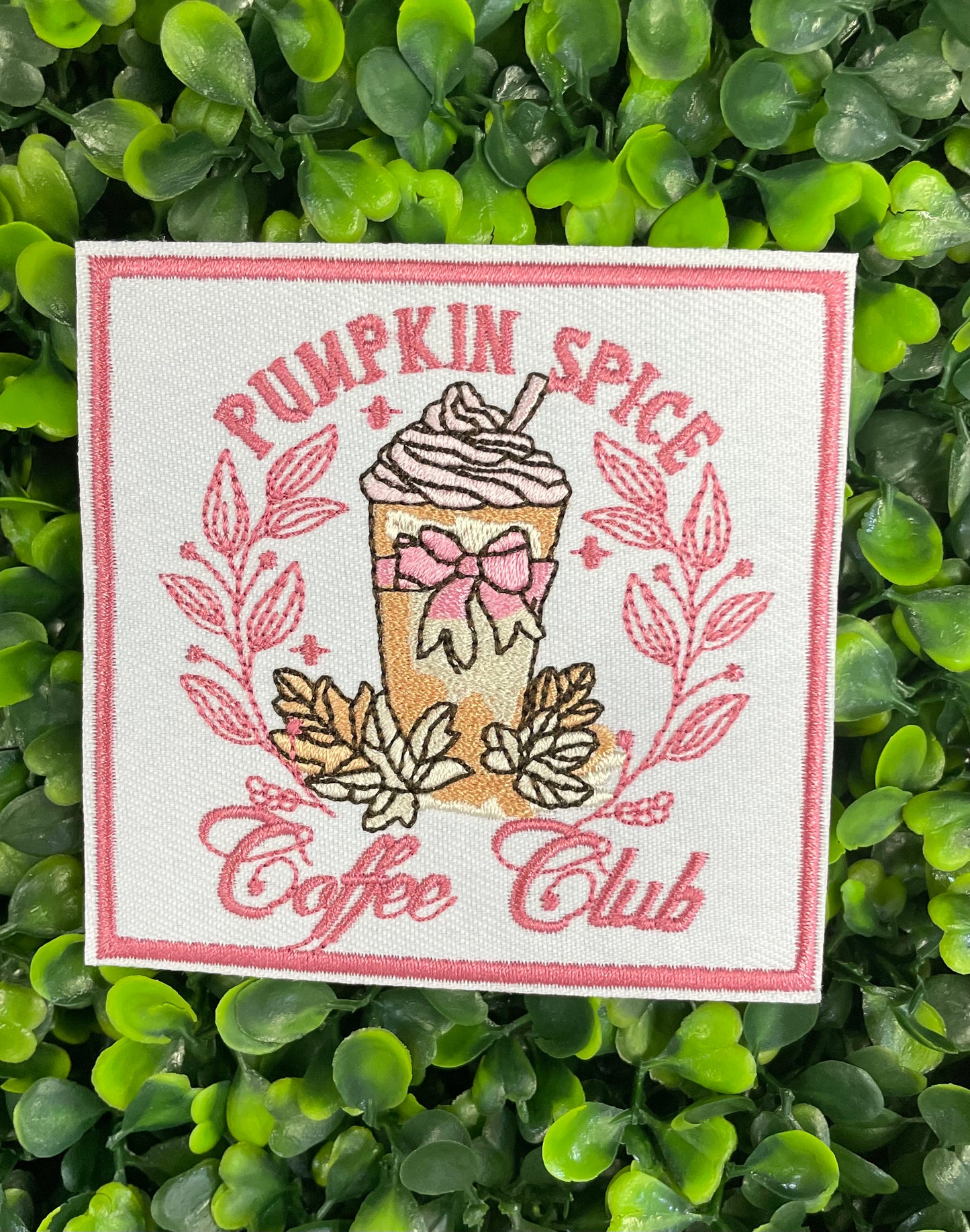 Sticker with pumpkin spice latte design and the text "pumpkin spice coffee club" placed on a green leafy backdrop