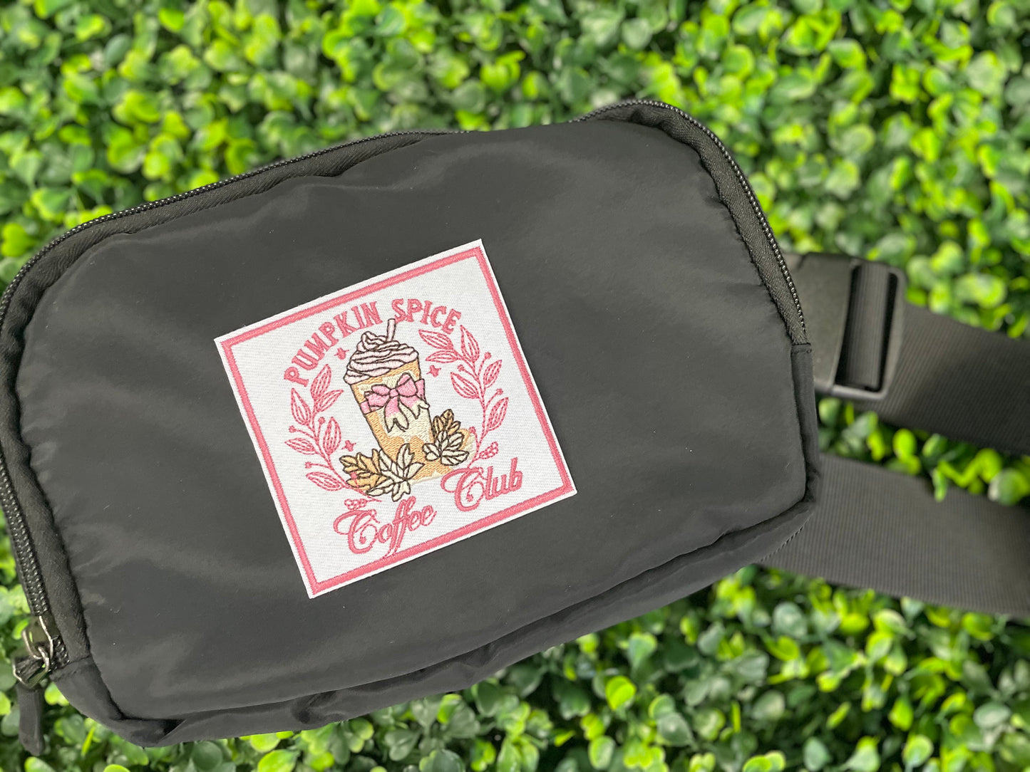 Sticker with pumpkin spice latte design and the text "pumpkin spice coffee club" placed on a black fanny pack
