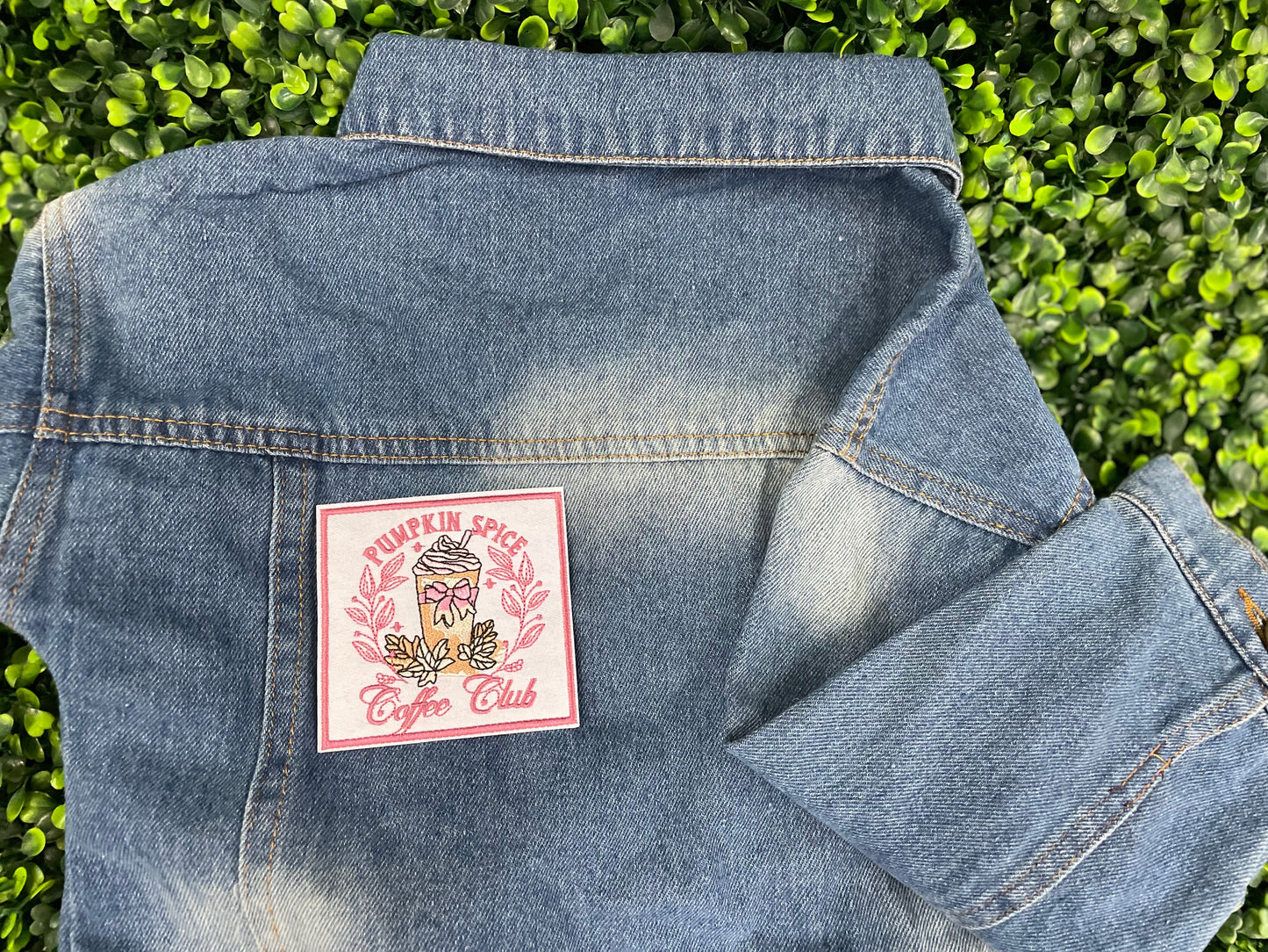Sticker with pumpkin spice latte design and the text "pumpkin spice coffee club" placed on a children's denim jean jacket