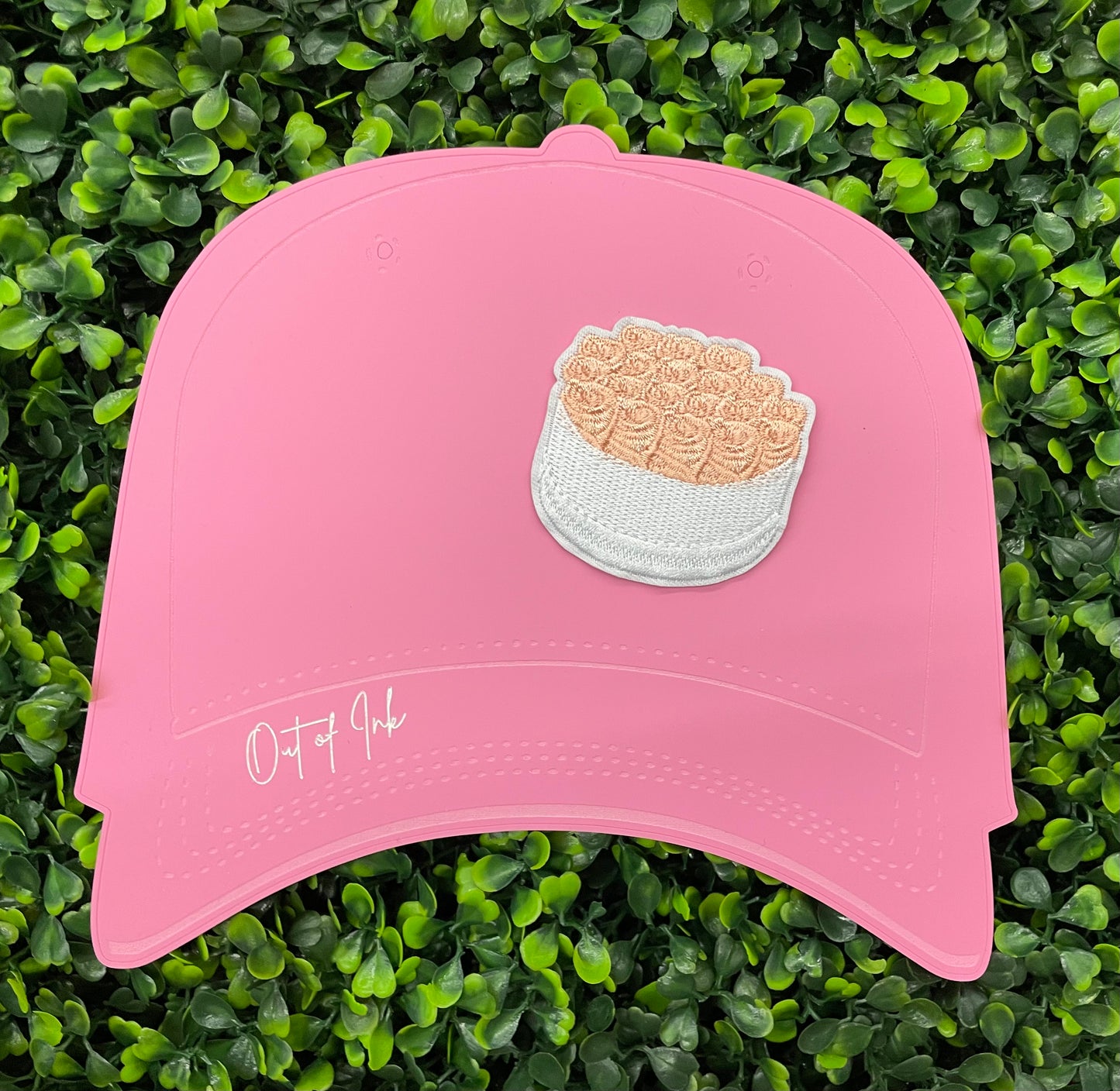An embroidered patch in the shape of a bundle of roses with pink petals and green leaves, placed on a pink hat
