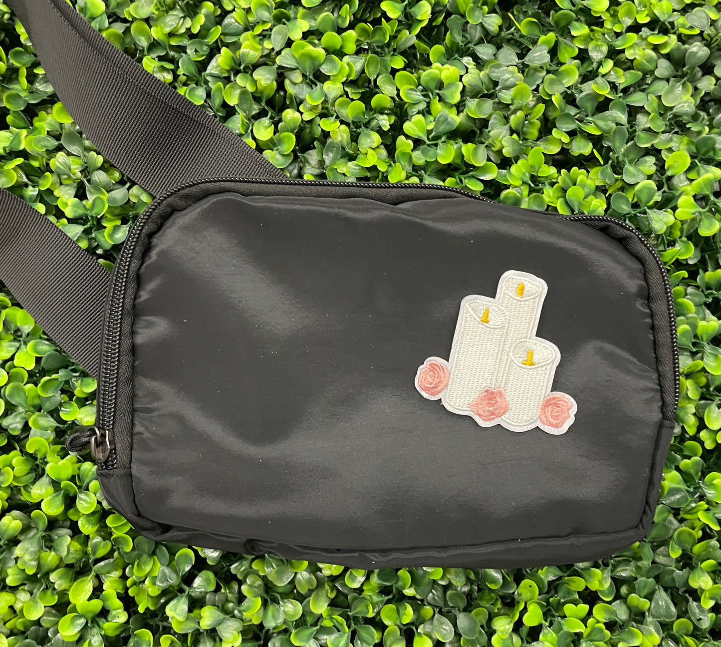 A patch with embroidered candles and roses in pink and yellow colors on a white background, placed on a black shoulder bag