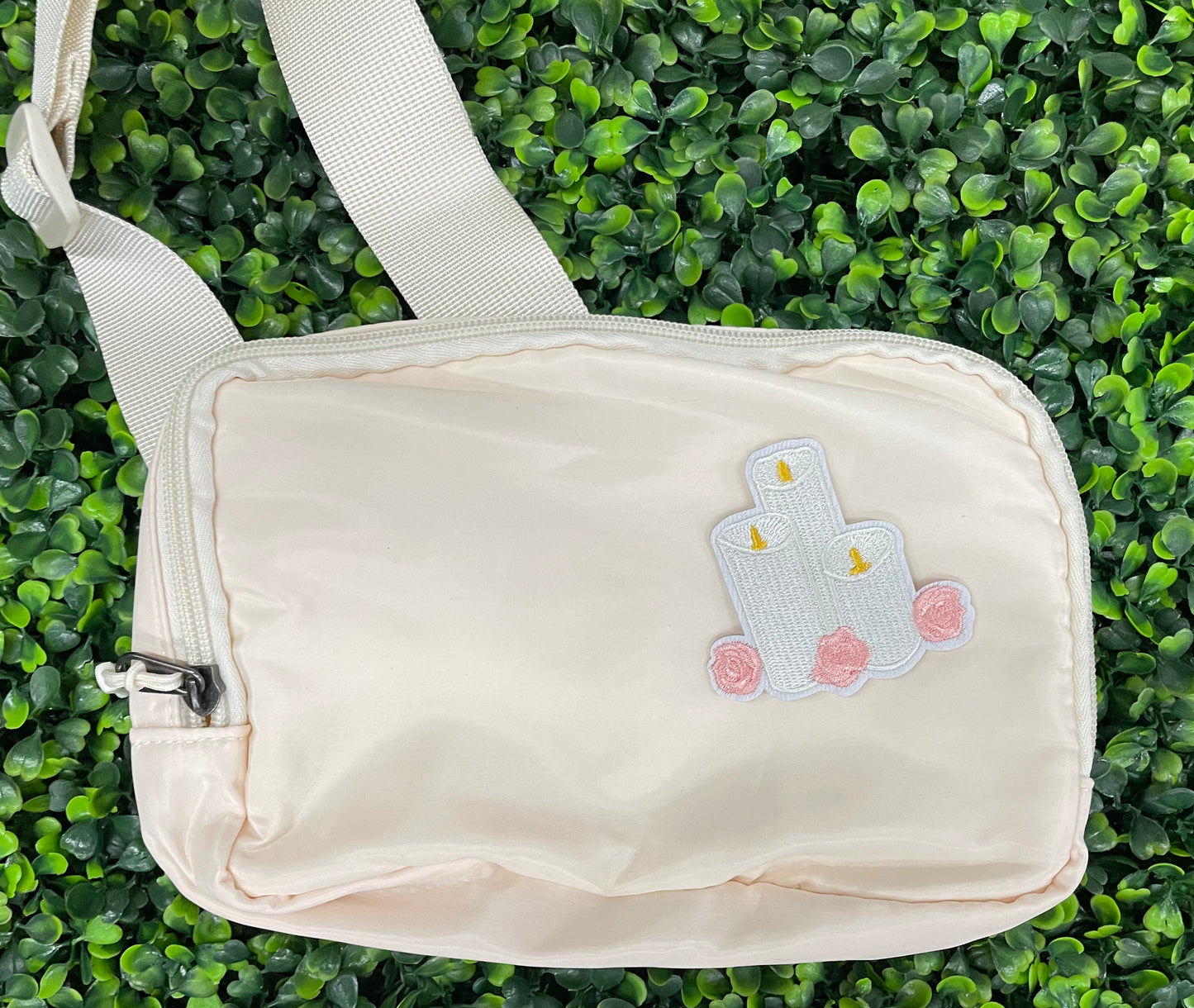 A patch with embroidered candles and roses in pink and yellow colors on a white background, placed on a white shoulder bag