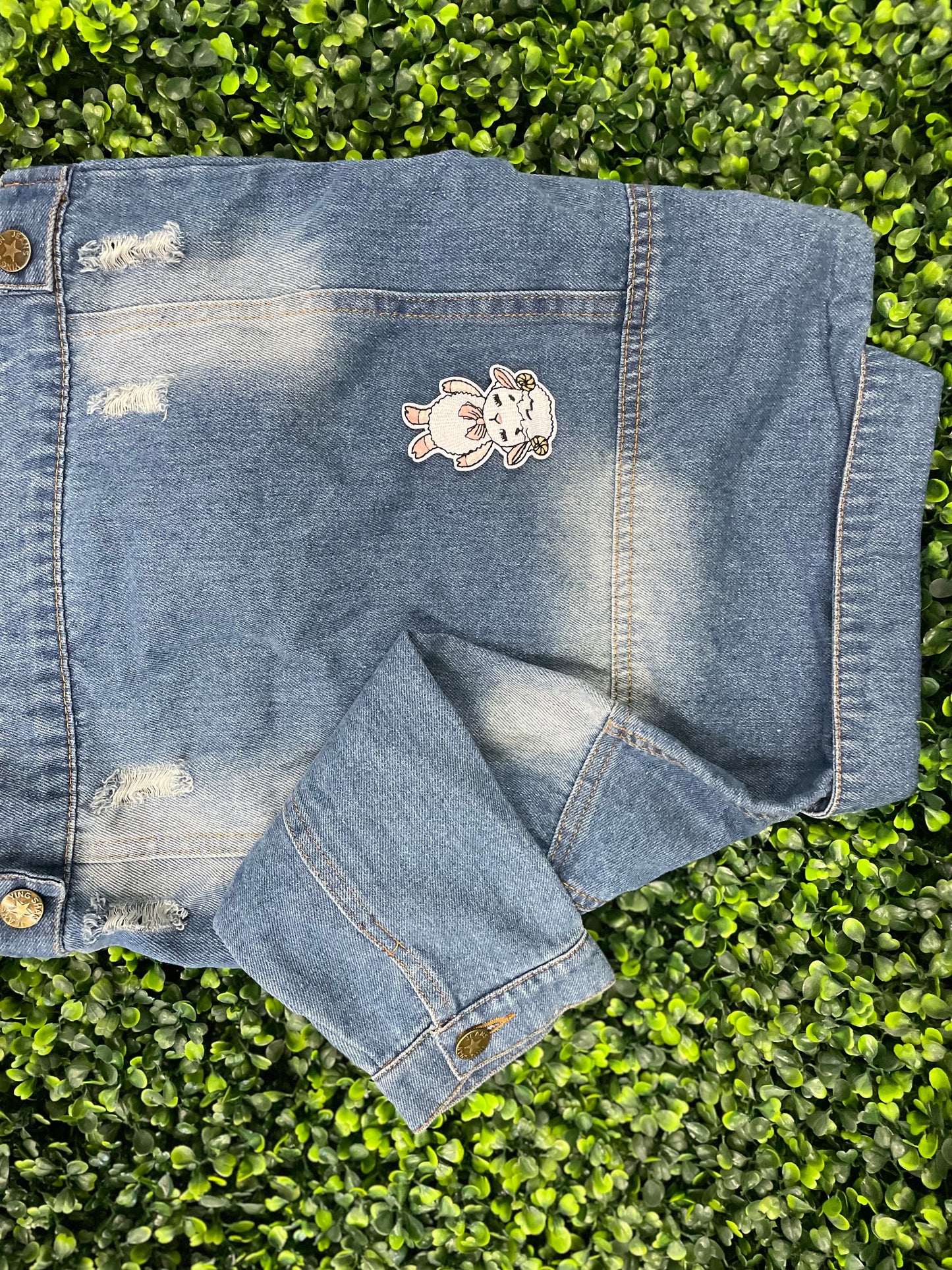 Patch of a cartoon lamb held against a children's denim jean-jacket