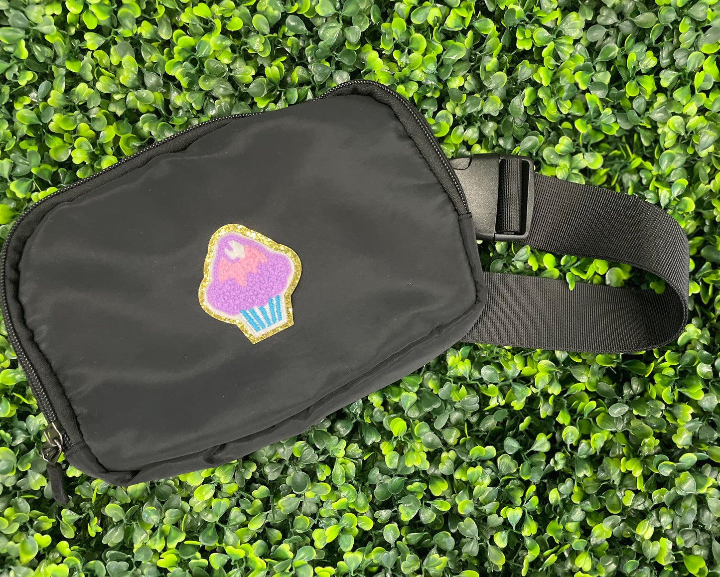 Decorative patch of a cupcake with pink and purple frosting, placed on a black fanny pack