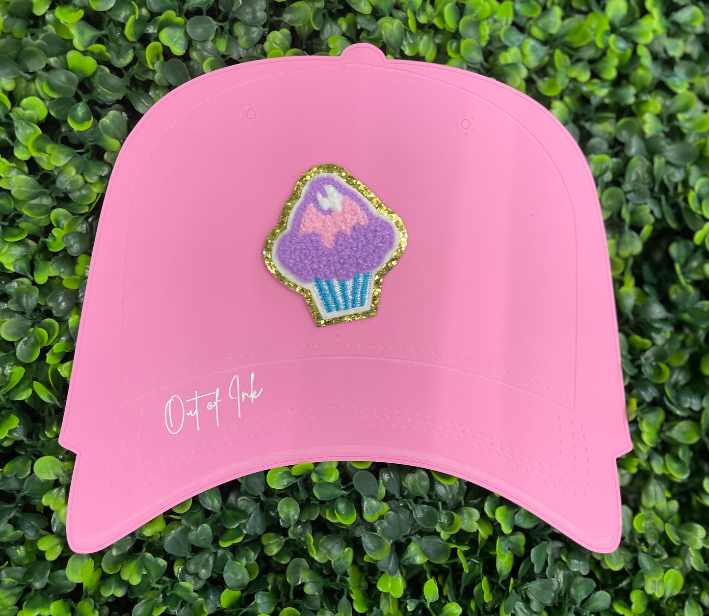 Decorative patch of a cupcake with pink and purple frosting, placed on a pink trucker hat graphic
