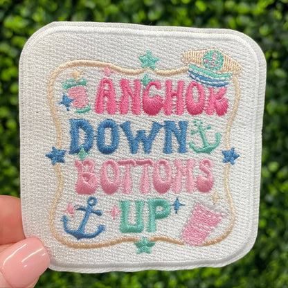 Embroidered patch with 'Anchors Down, Buttons Up' text held against a green leafy background
