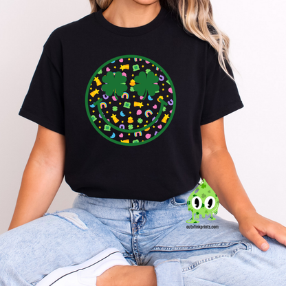 Front view of a black t-shirt with a smiley face design featuring clovers, celebrating St. Patrick's Day.