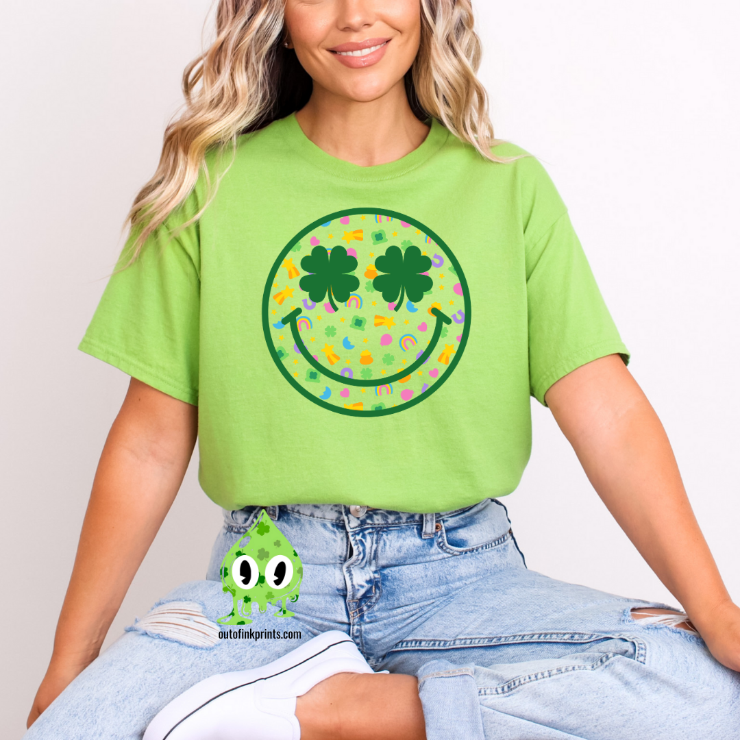 Front view a green t-shirt with a smiley face design featuring clovers, celebrating St. Patrick's Day.