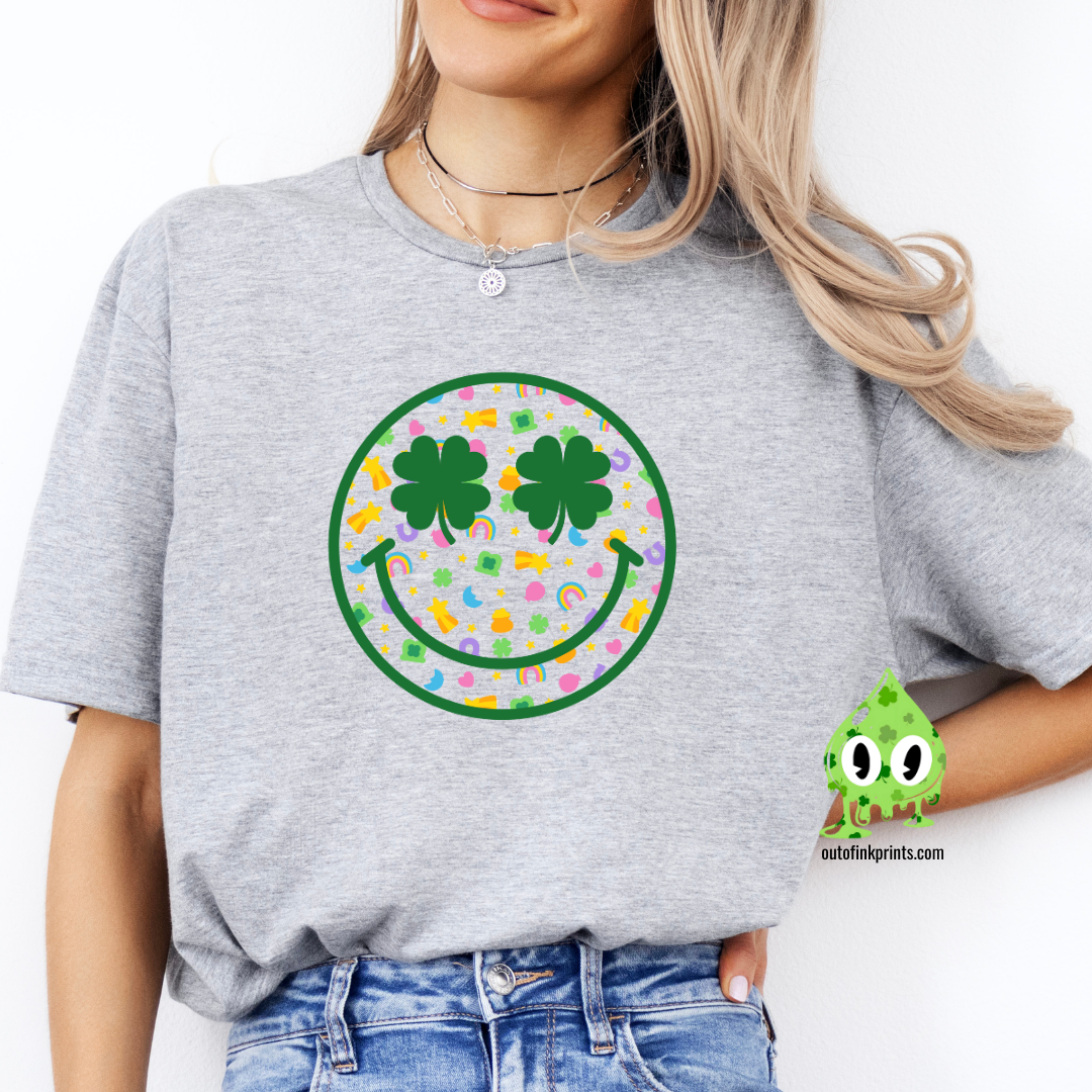Front view of a gray t-shirt with a smiley face design featuring clovers, celebrating St. Patrick's Day.