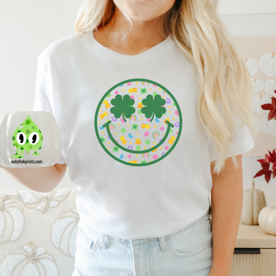A person wearing a white t-shirt with a graphic of a smiley face surrounded by a rainbow checkered pattern and clover leaves.